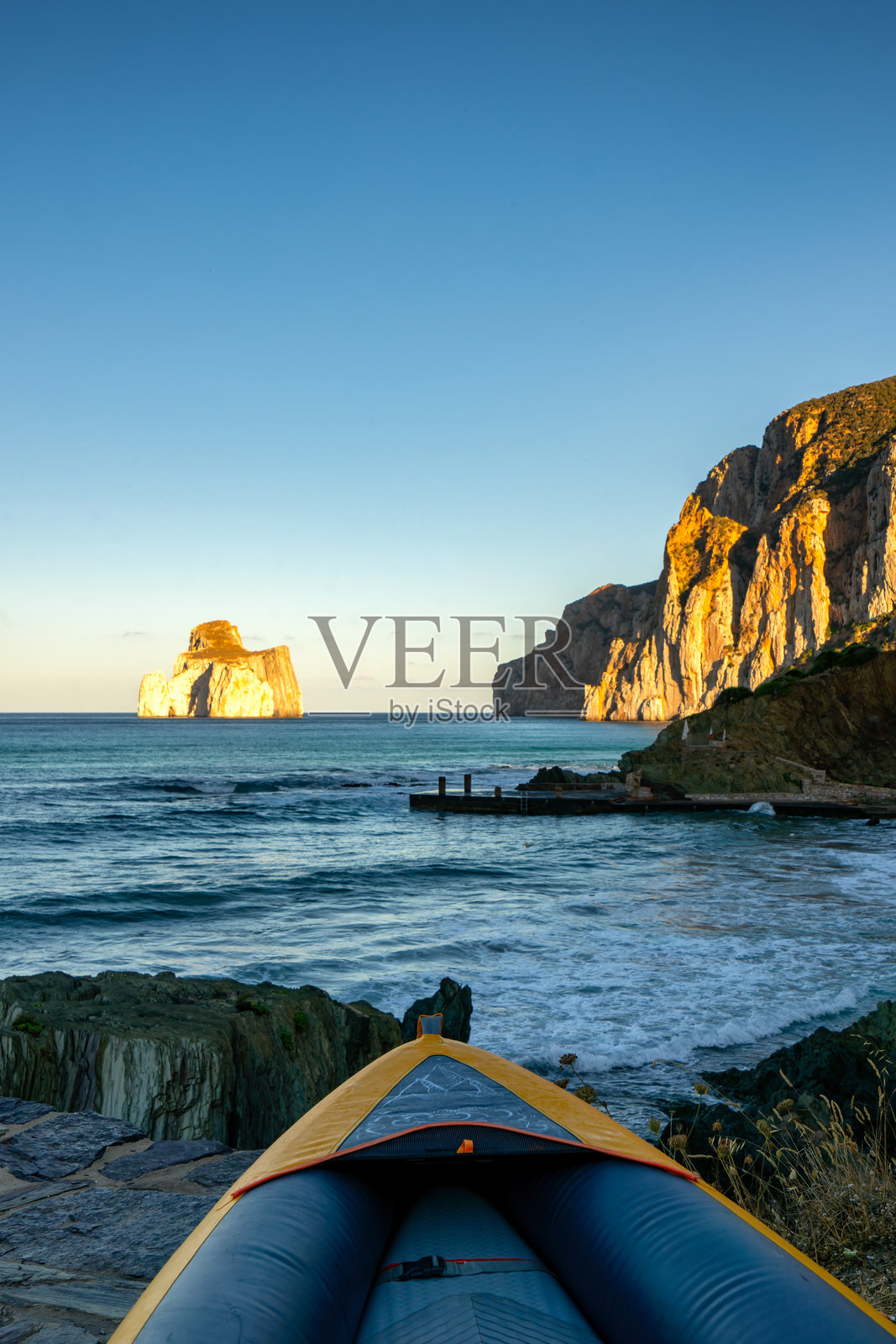 日出时分,在意大利撒丁岛马苏阿海滩,乘坐充气皮划艇探索,背景是糖面包山照片摄影图片