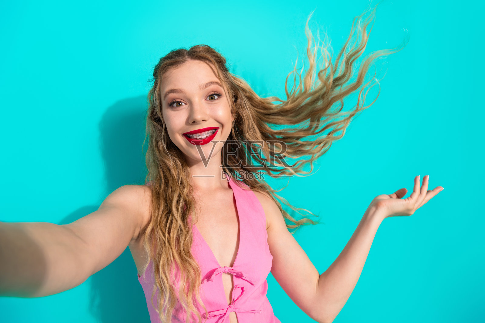 年轻女子身穿粉色上衣,笑容灿烂,时尚自拍风格肖像,背景为蓝绿色,展现无忧无虑的别致魅力照片摄影图片