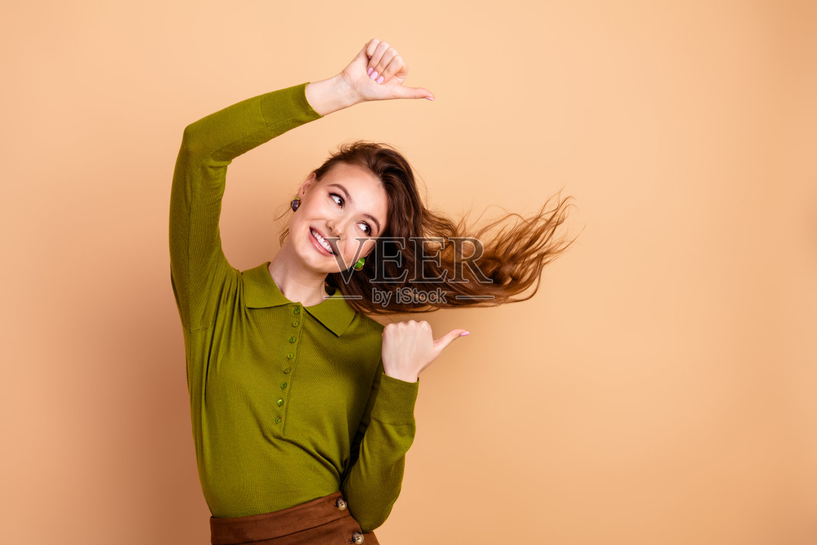 身穿绿色上衣、长发飘逸的年轻时尚女模特,在米色背景前,展现出愉悦、趣味、时尚、生活方式和休闲别致的风格照片摄影图片