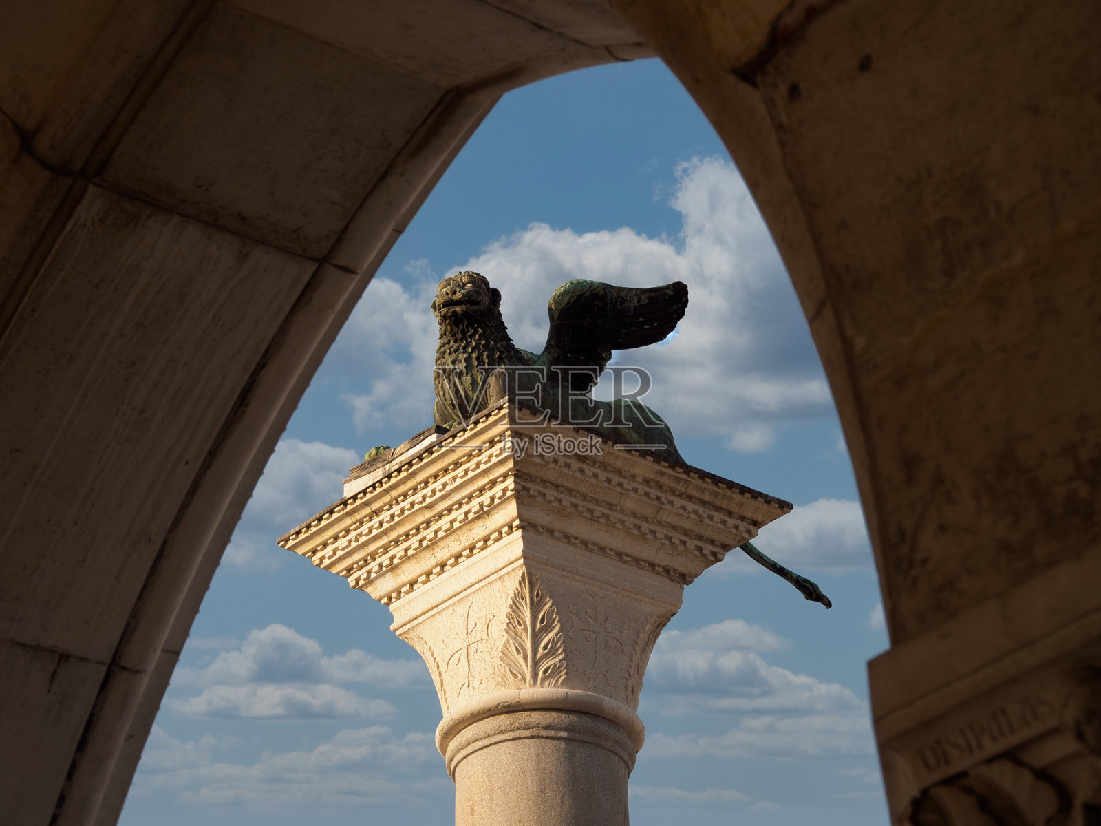 威尼斯雄狮石柱与天空,戏剧性低角度仰拍,飞翼的威尼斯雄狮坐落于石柱顶端,古老的石拱门框景,背景是明亮多云的蓝天。照片摄影图片