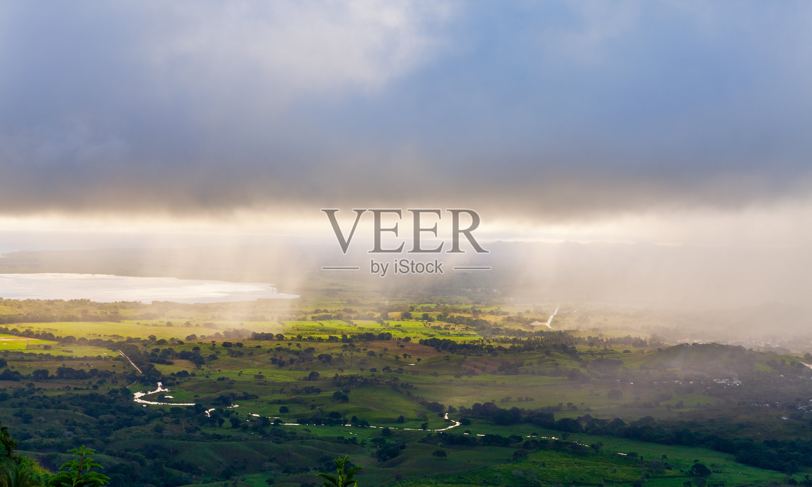 绿色的田野、蜿蜒的道路和朦胧的阳光照射下的开阔山谷风景照片摄影图片