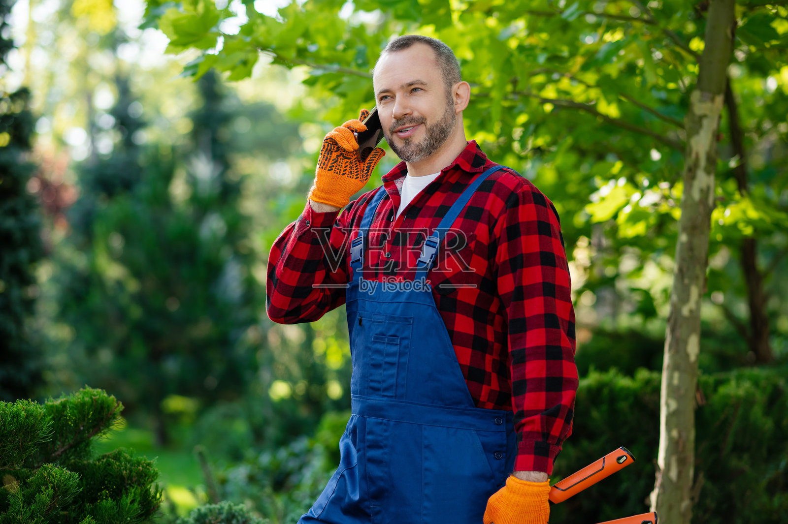 穿着制服的男性园艺师在绿色花园里用手机沟通照片摄影图片