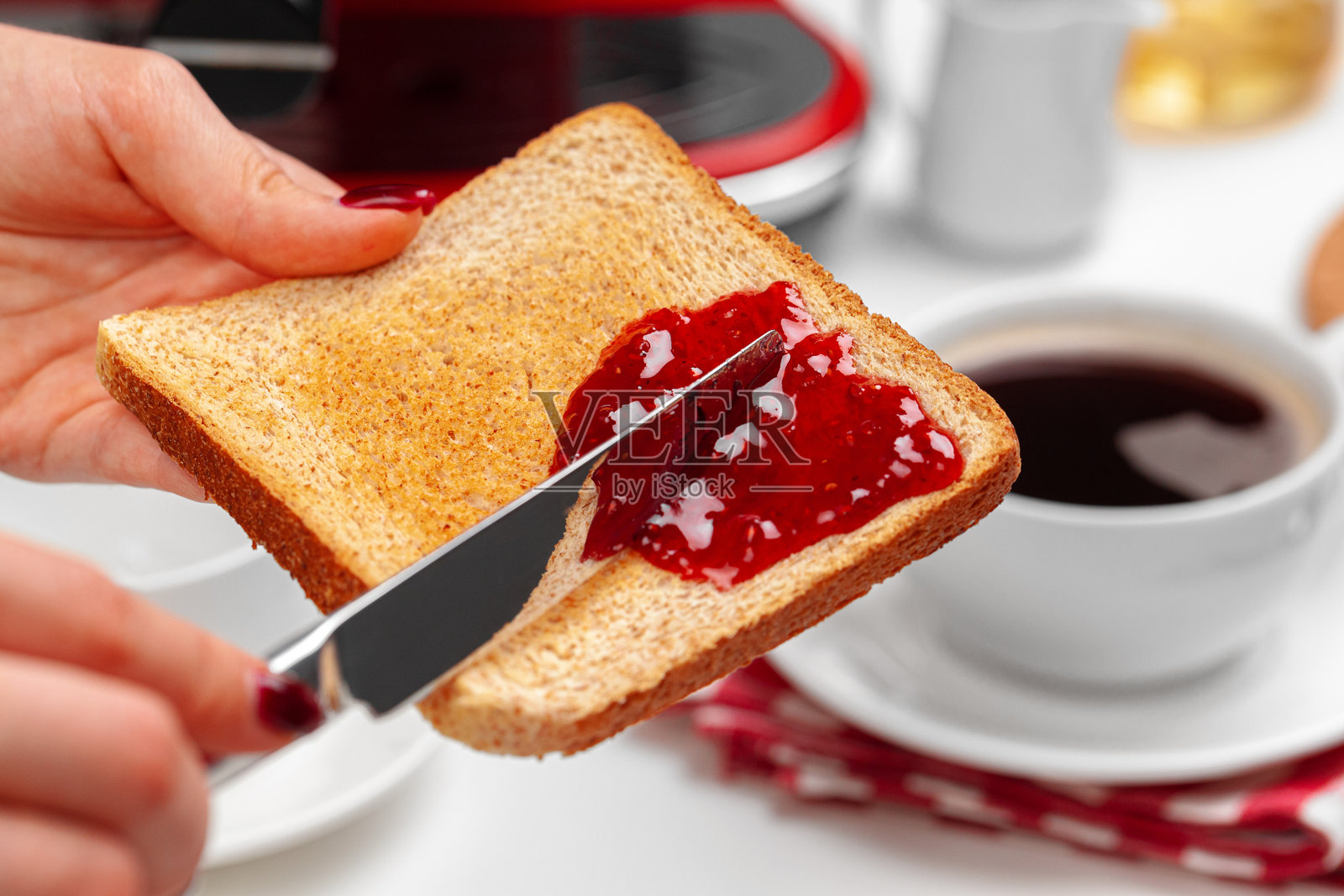 女性的手将草莓酱涂抹在烤好的吐司上照片摄影图片