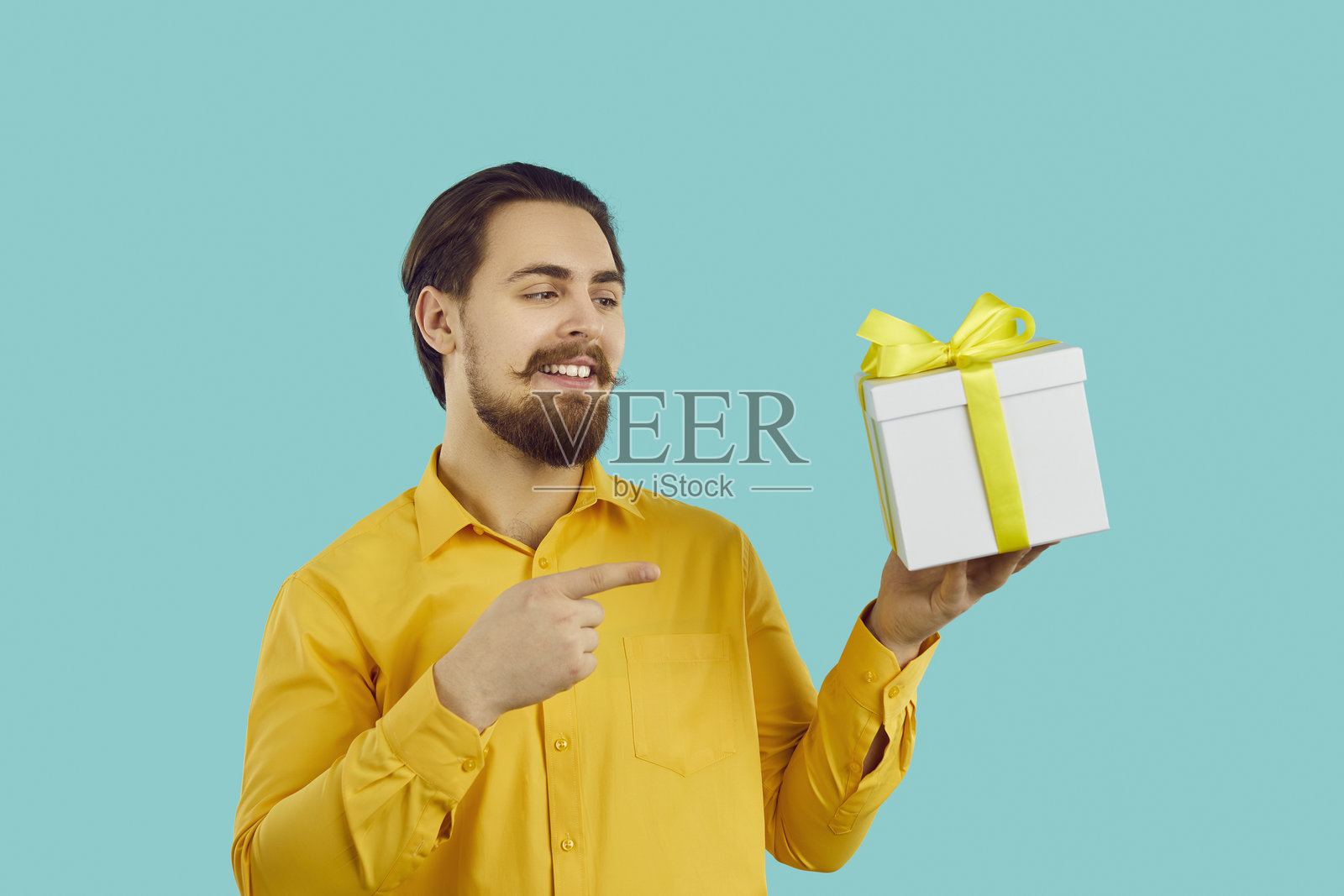 一位快乐迷人的男士手持礼物,在浅蓝色背景下提供特别节日优惠。照片摄影图片