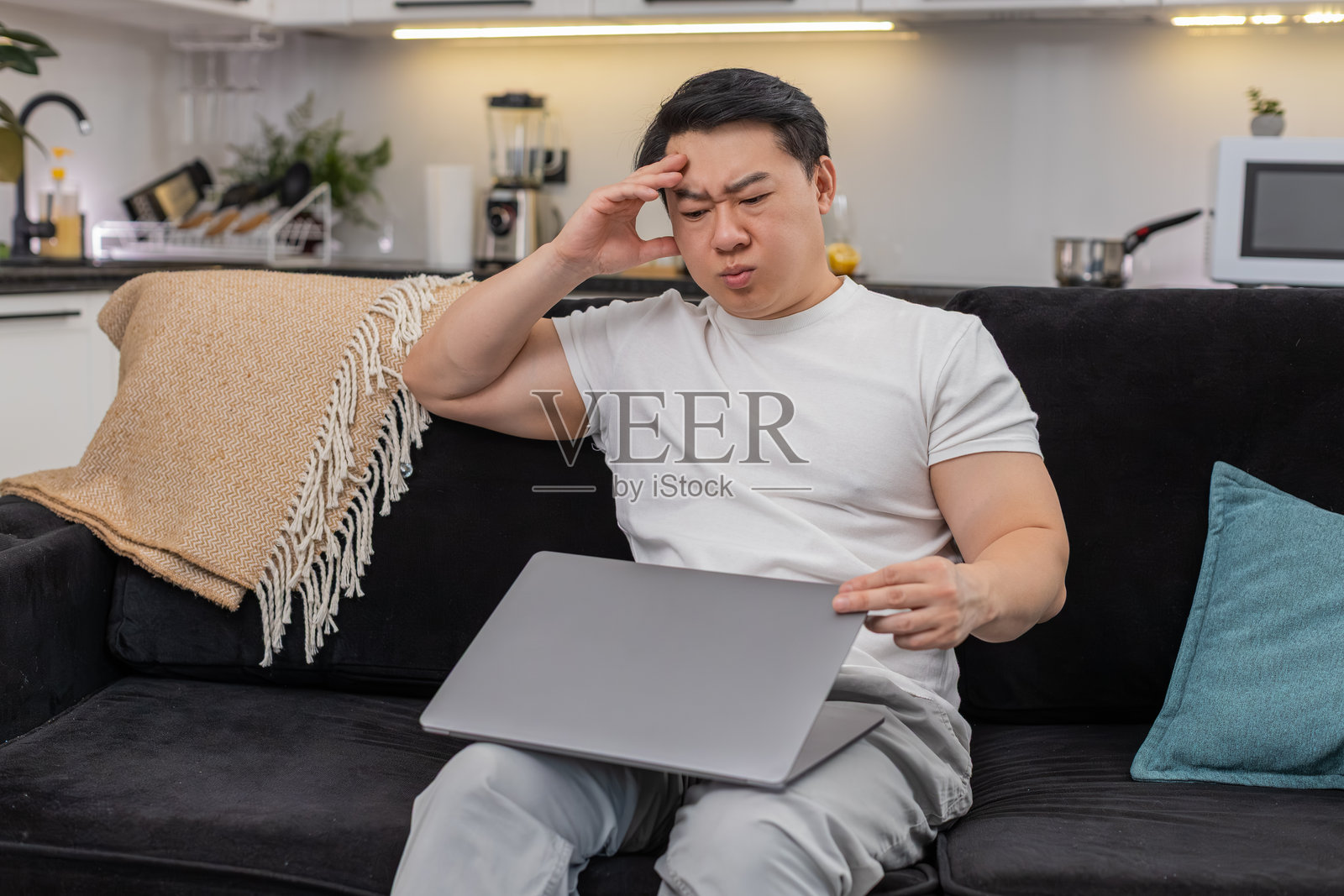 一名亚洲男子疲惫地合上笔记本电脑,挥手表示足够了,闭眼片刻,然后放松地向后靠去。照片摄影图片