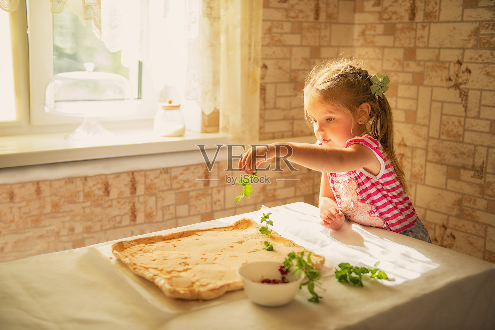 一个小女孩用薄荷叶和覆盆子装饰蛋白酥卷。它象征着童年、烹饪、健康饮食和家庭传统。照片摄影图片