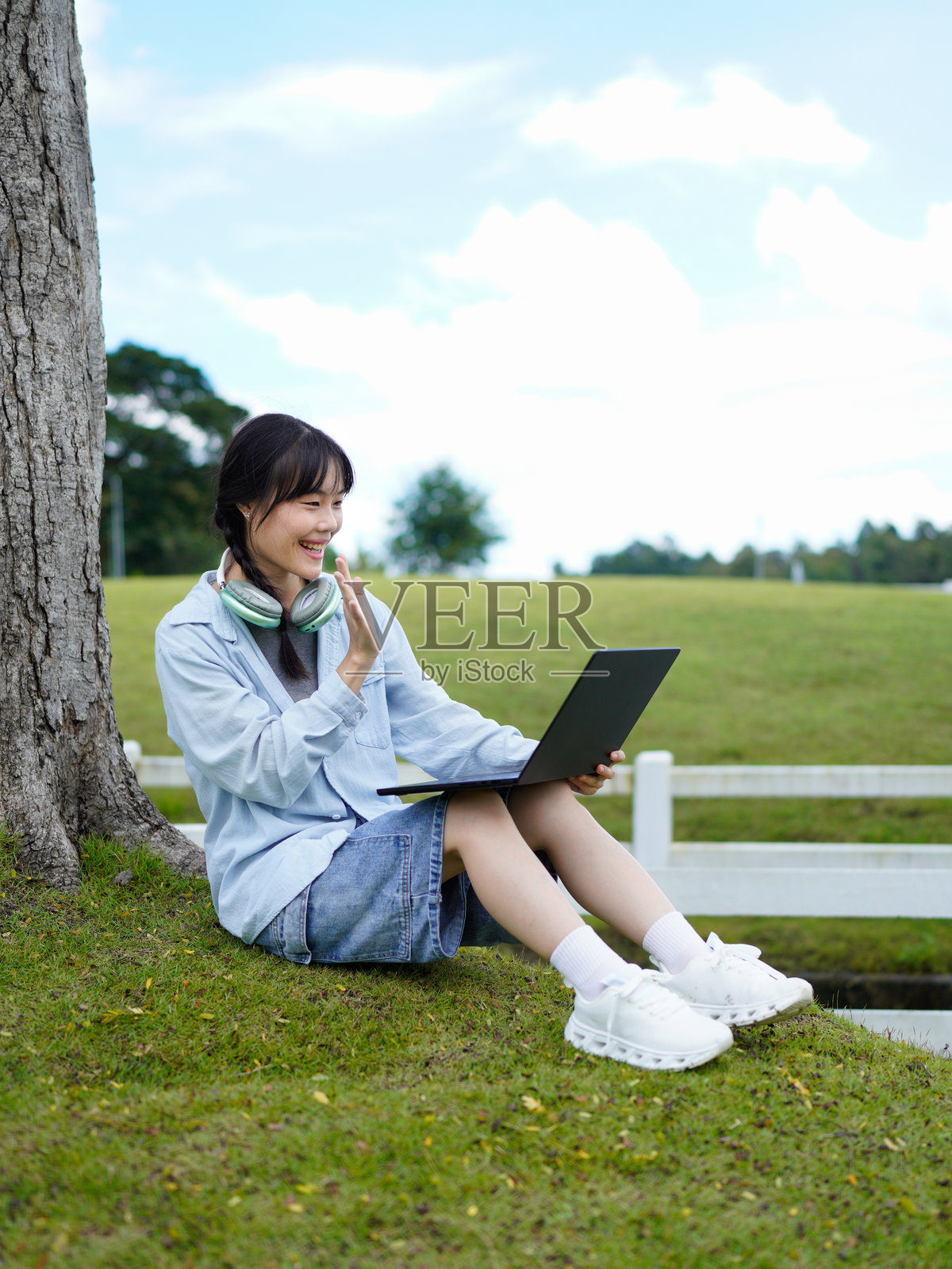 一位年轻的亚洲自由职业者在公园里专注地使用笔记本电脑和智能手机,享受着户外的清新空气和自然美景,身处宁静的户外环境。照片摄影图片