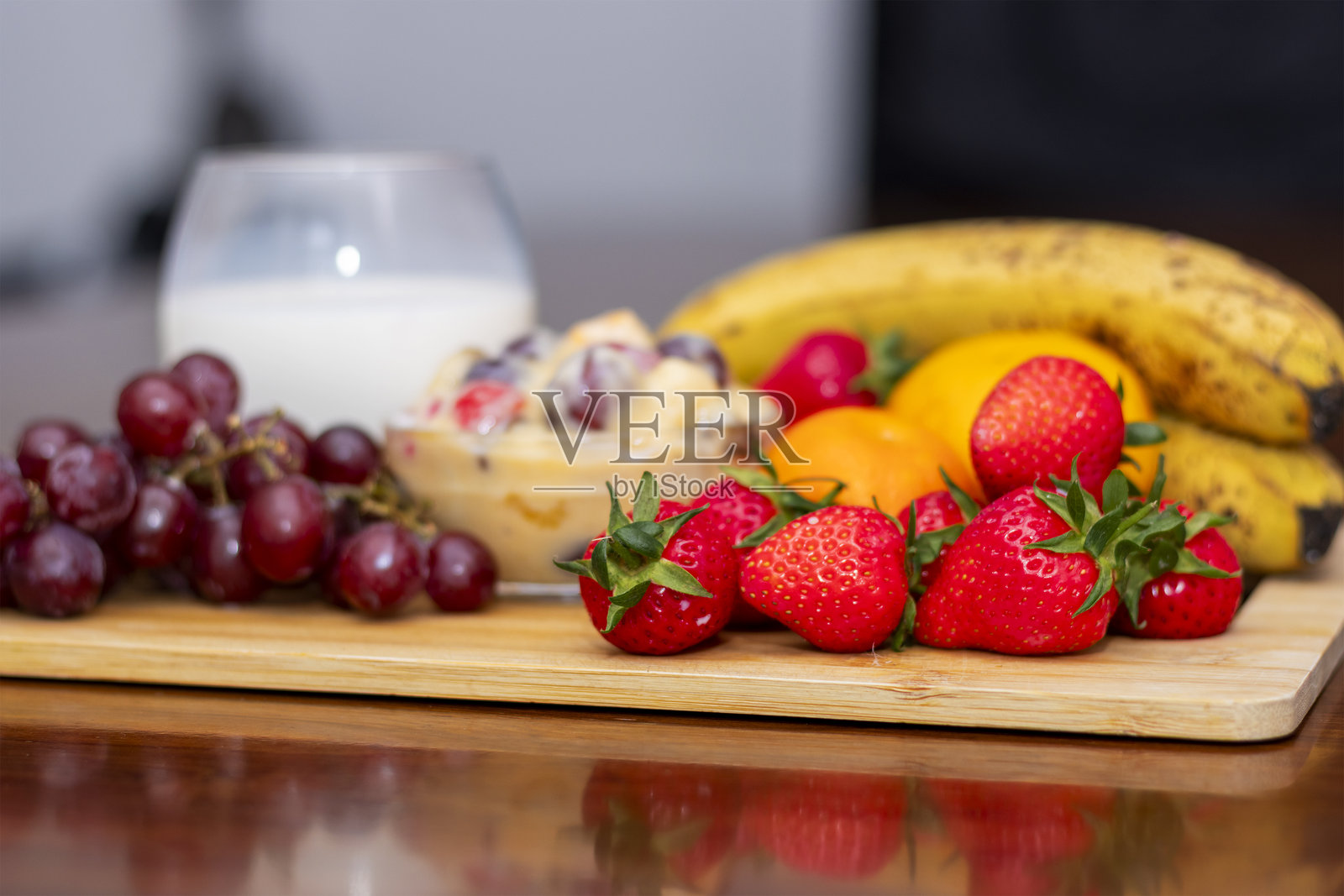 木板上的新鲜水果沙拉,配有牛奶、葡萄、草莓、香蕉和橙子照片摄影图片