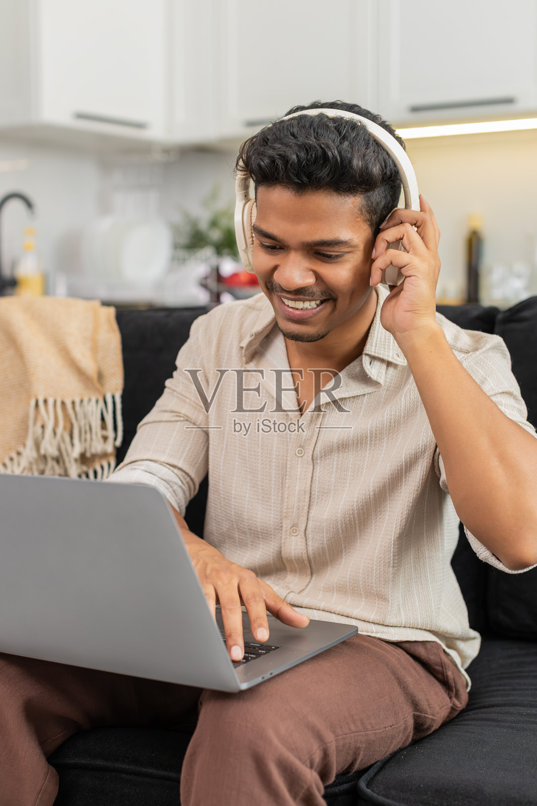 印度男子戴着无线耳机,在笔记本电脑上编辑短视频,自由职业者面带赞许的微笑。照片摄影图片