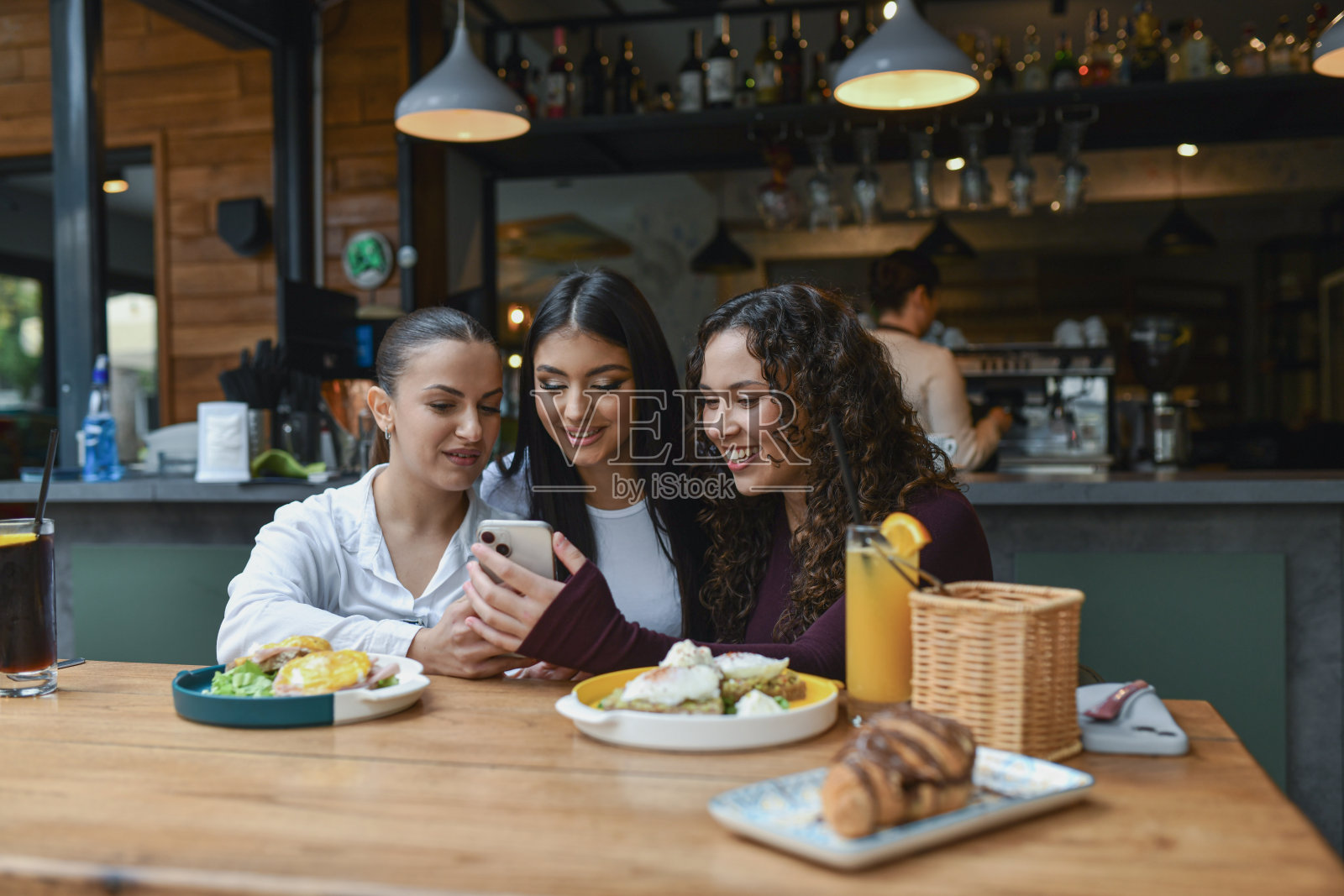 三位朋友在休息酒吧享用早餐,同时在手机上分享照片照片摄影图片