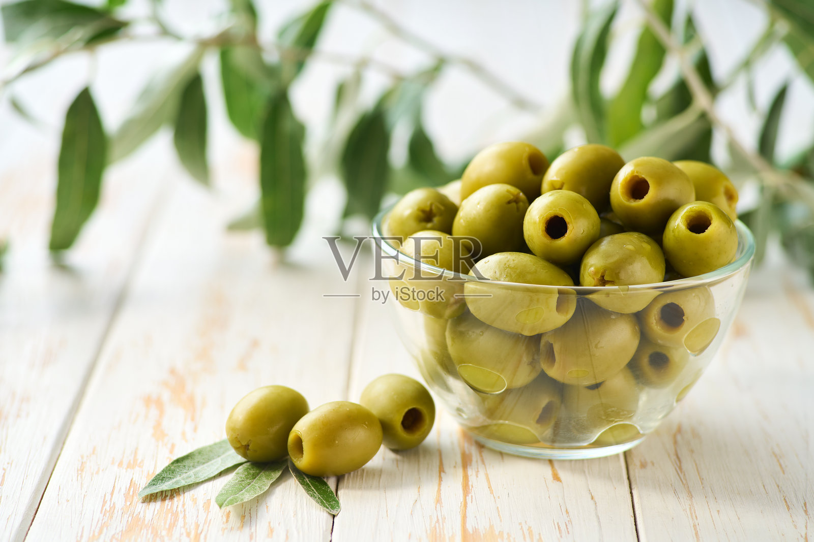 白色木桌上透明玻璃碗里的去核橄榄,焦点选择性。腌制去核橄榄。照片摄影图片