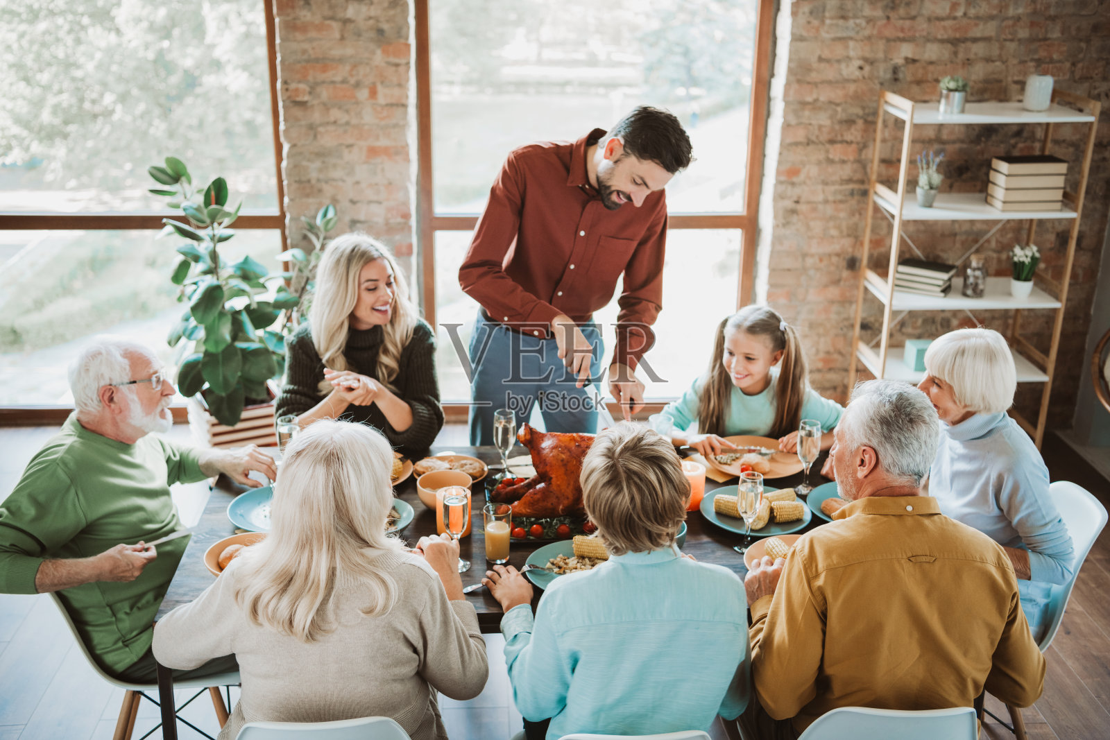 祖父母、父母和孩子们围坐在一张长桌旁,共享丰盛的感恩节大餐,充满欢声笑语、美食与爱。照片摄影图片