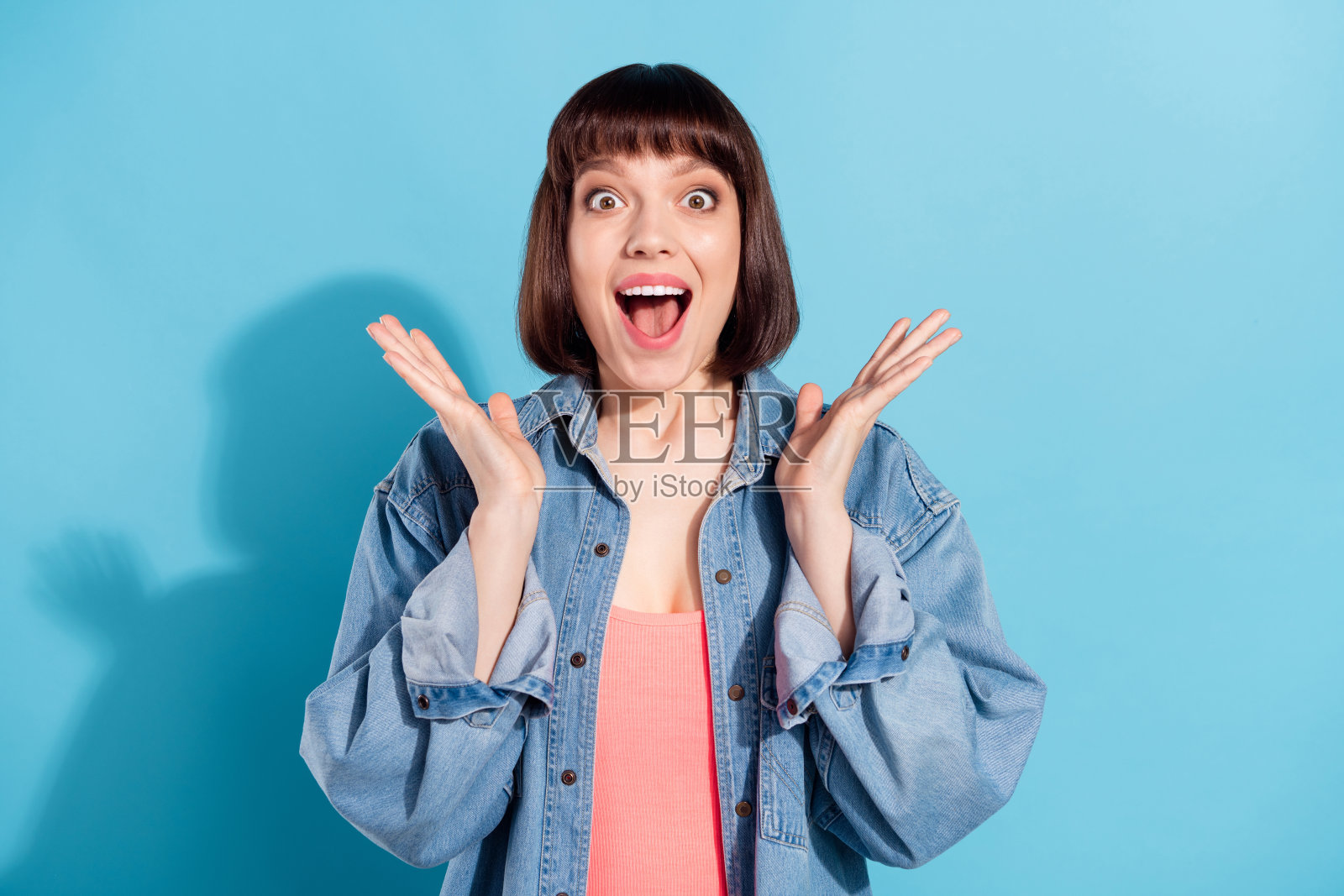 一位迷人的、开心的、惊讶的棕发女孩的肖像,对好消息做出反应,背景是明亮的蓝色照片摄影图片