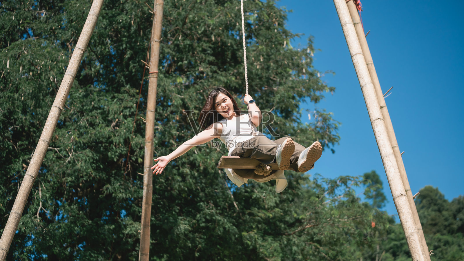 阳光明媚的公园里,一个快乐的孩子正坐在木制秋千上荡秋千,周围环绕着绿树,天空湛蓝,画面充满了幸福与自由的感觉。照片摄影图片