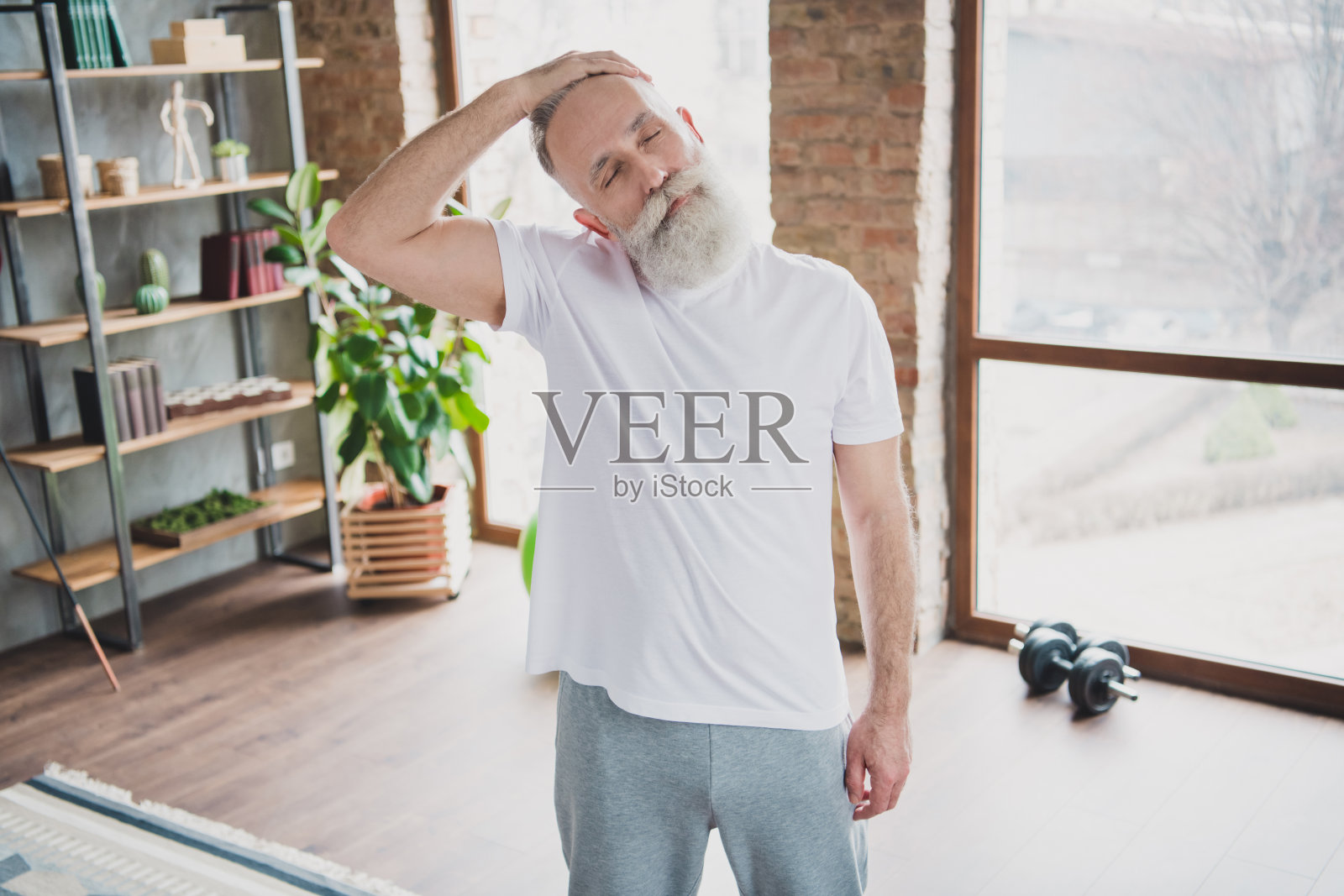 照片:一位心情愉悦、充满活力的爷爷在家中锻炼,伸展脖子,享受居家训练的时光。照片摄影图片