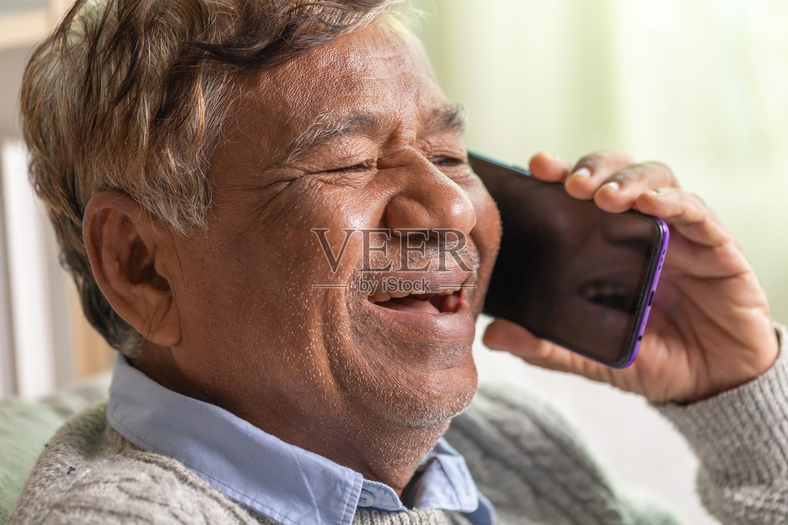 一位快乐的老人正在家里使用智能手机大笑。照片摄影图片