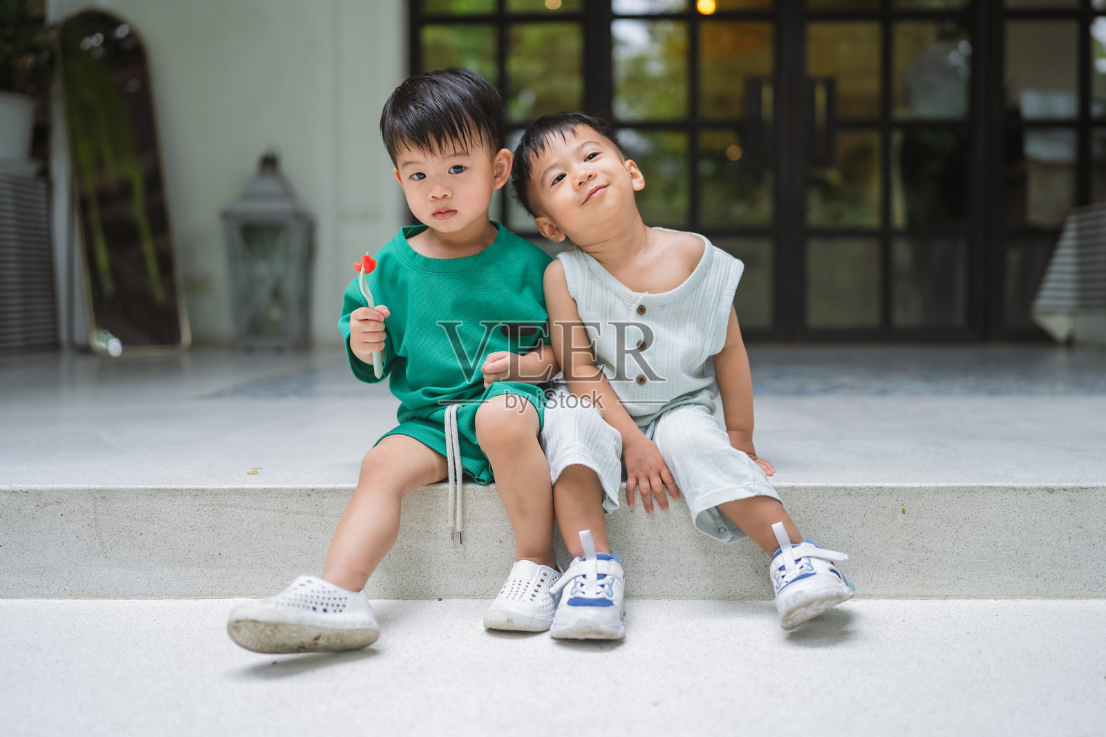 两个开朗的亚洲小男孩在阳光明媚的周末下午坐在一起,在假期里放松地开怀大笑。在温暖的日光环绕下,他们在自然中享受着友谊、快乐和嬉戏的童年时光。照片摄影图片