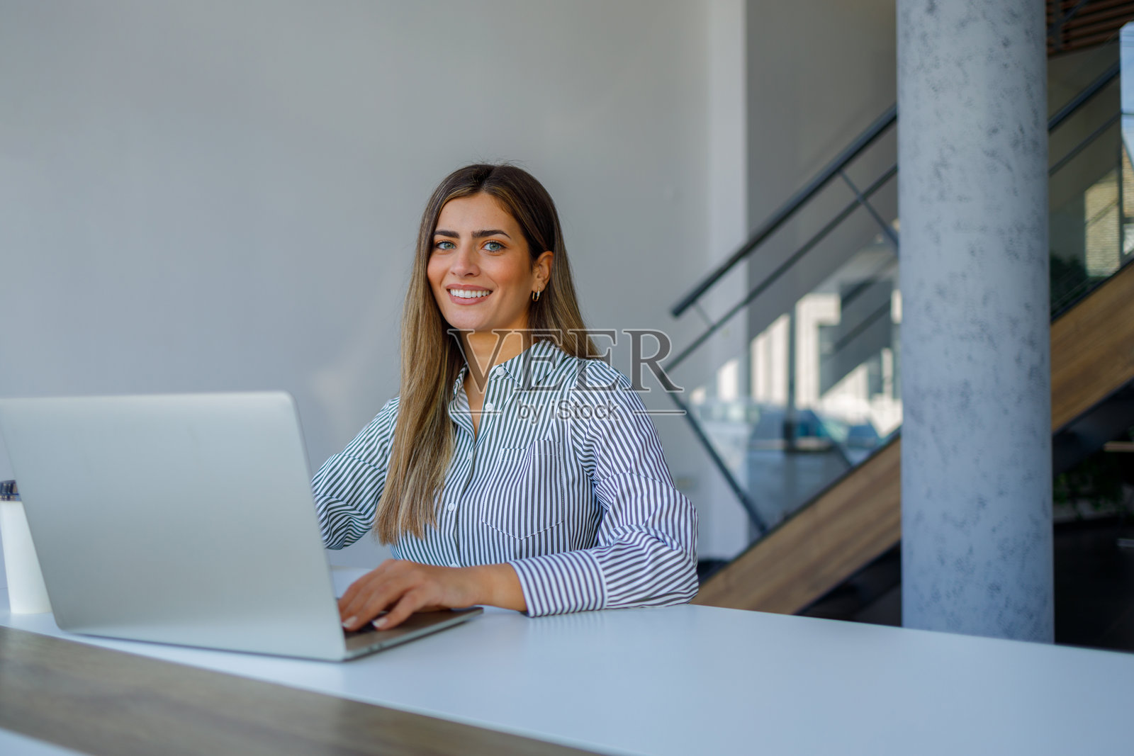 一位面带微笑的女性在现代办公室使用笔记本电脑工作,通过远程办公取得成功和高效照片摄影图片