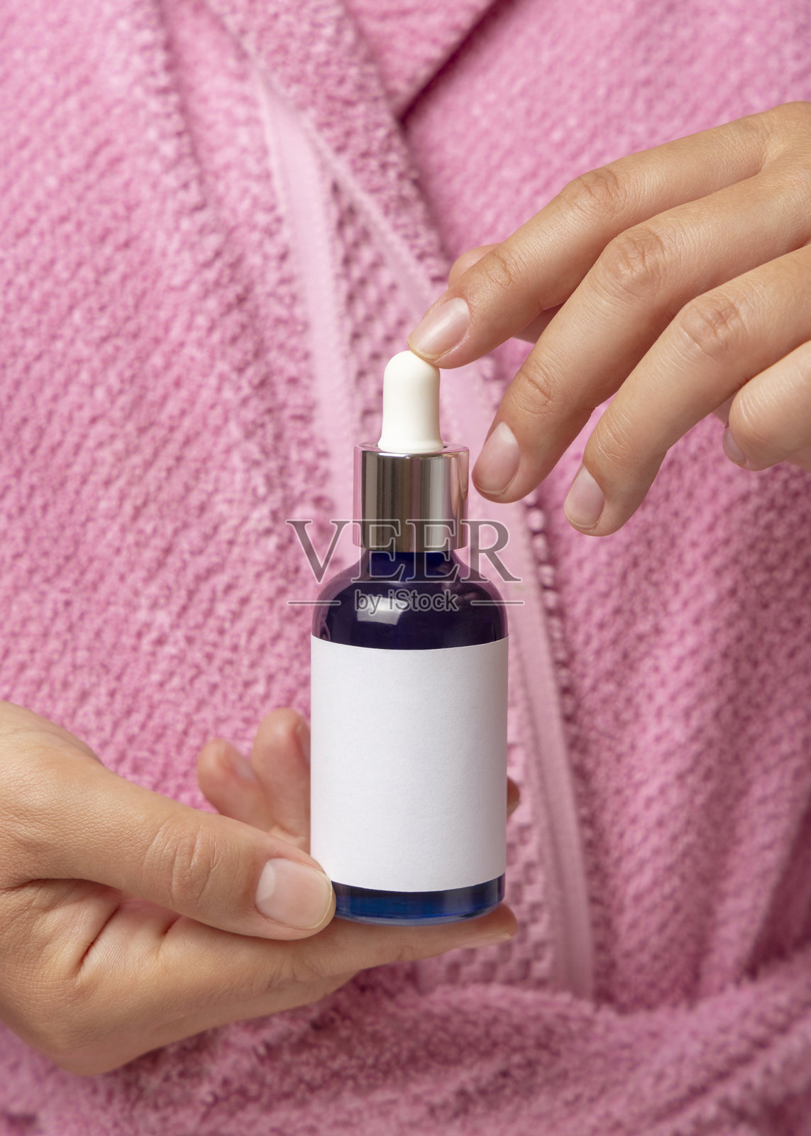 粉色浴袍女子手持带标签的蓝色滴管瓶,化妆品模型特写照片摄影图片