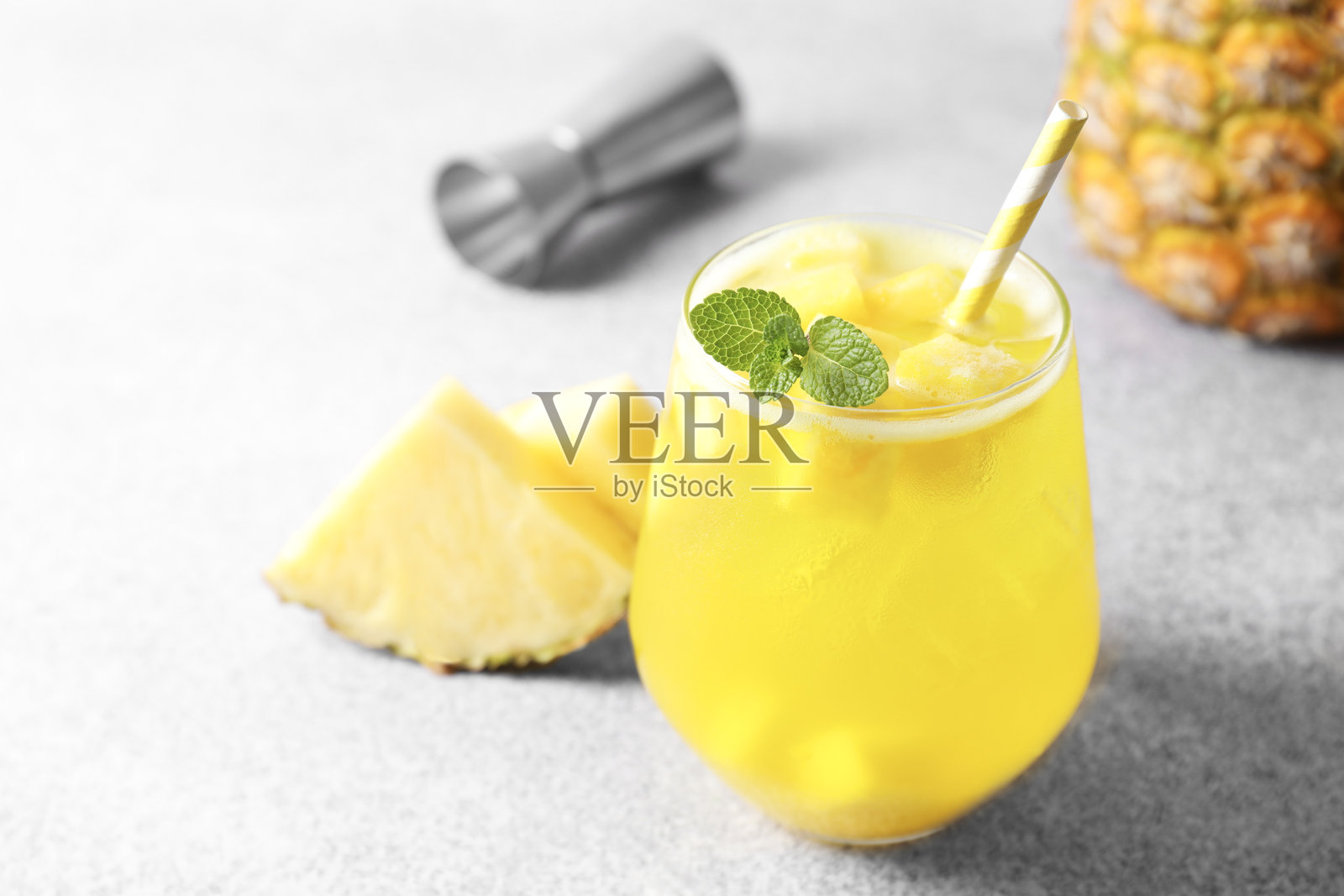 玻璃杯中放有美味的菠萝鸡尾酒和薄荷叶,置于灰色桌面上,特写镜头照片摄影图片
