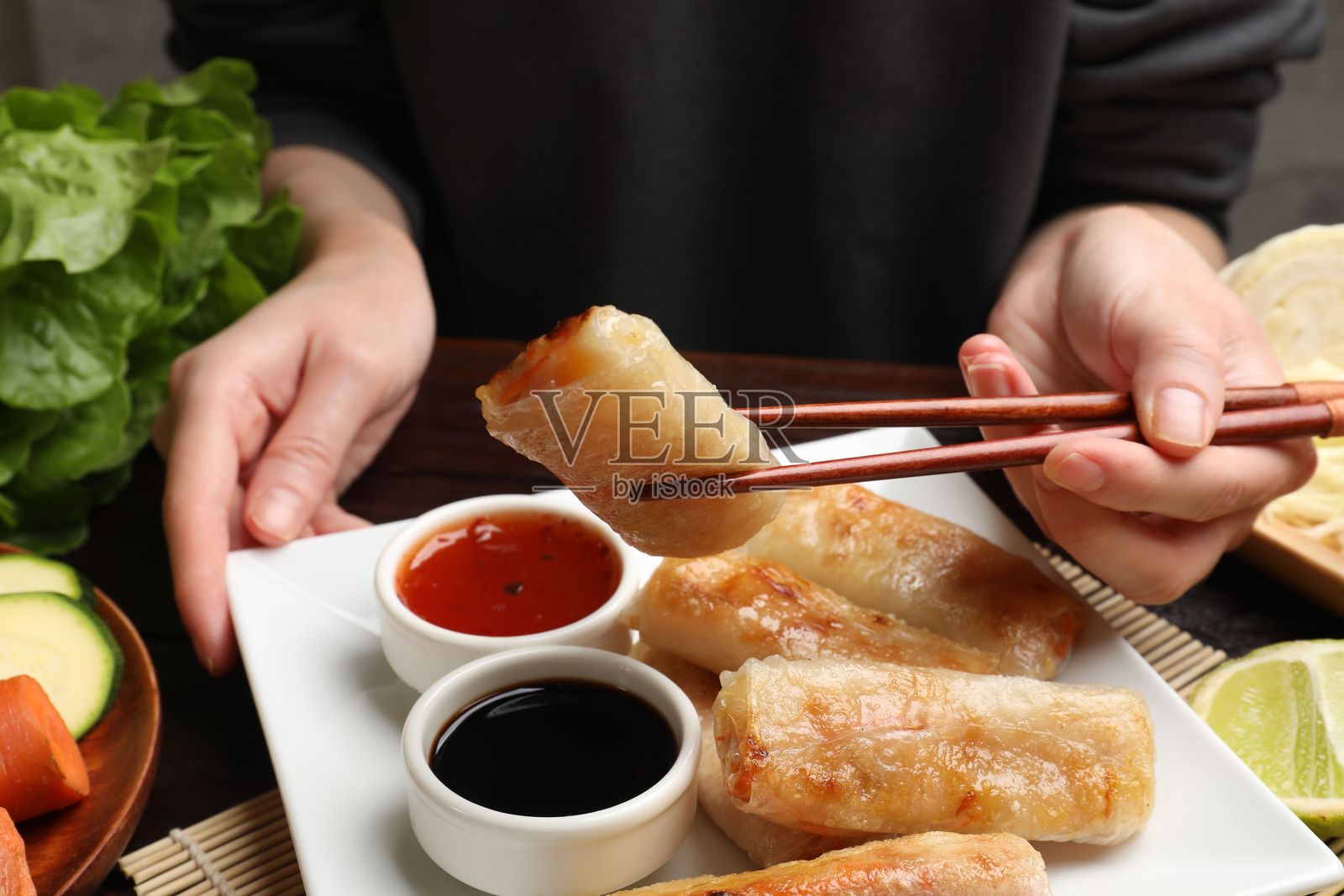 特写:女子在餐桌旁享用美味的炸春卷照片摄影图片