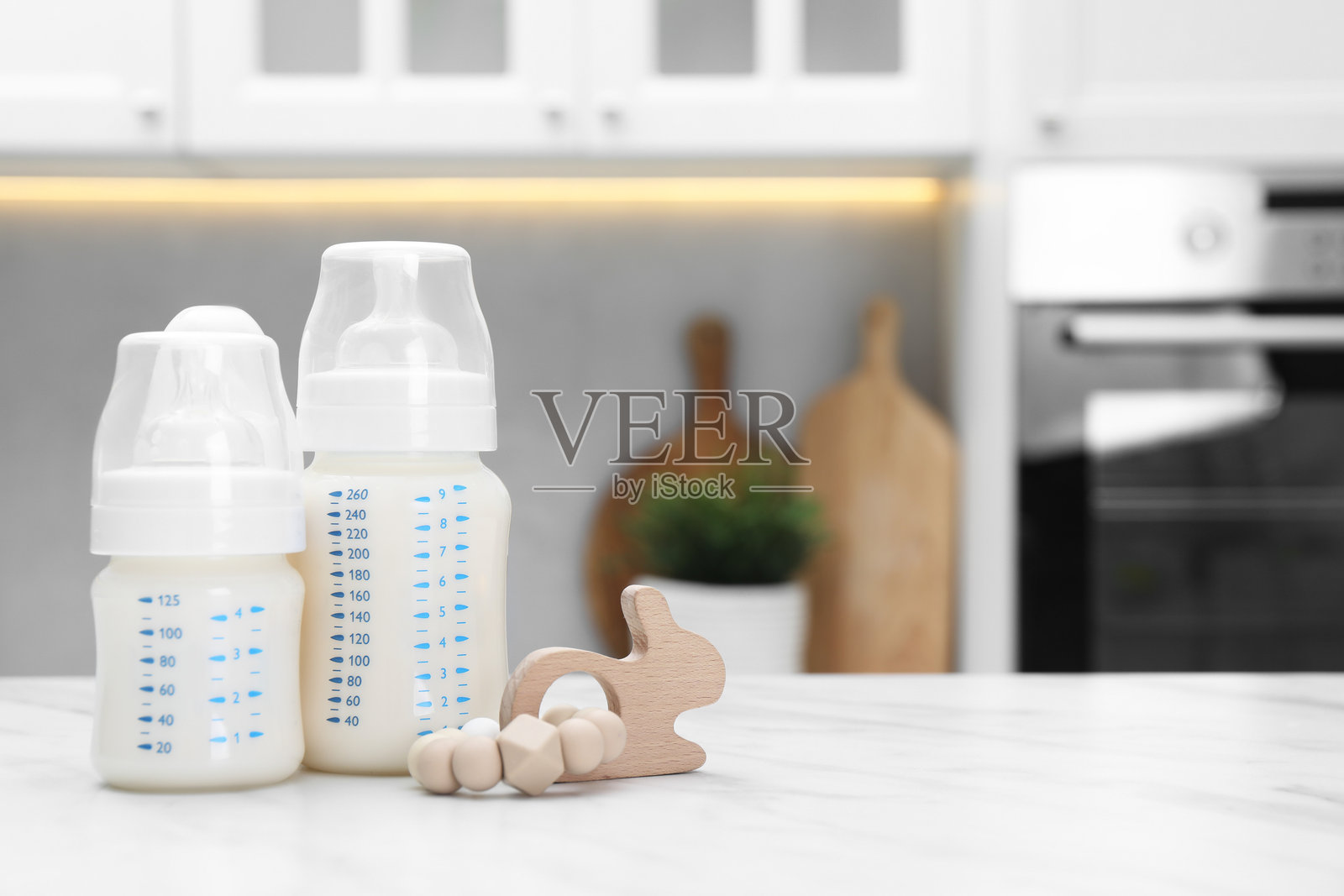 白色桌子上放着奶瓶、牛奶和玩具,室内拍摄,留有文字空间照片摄影图片
