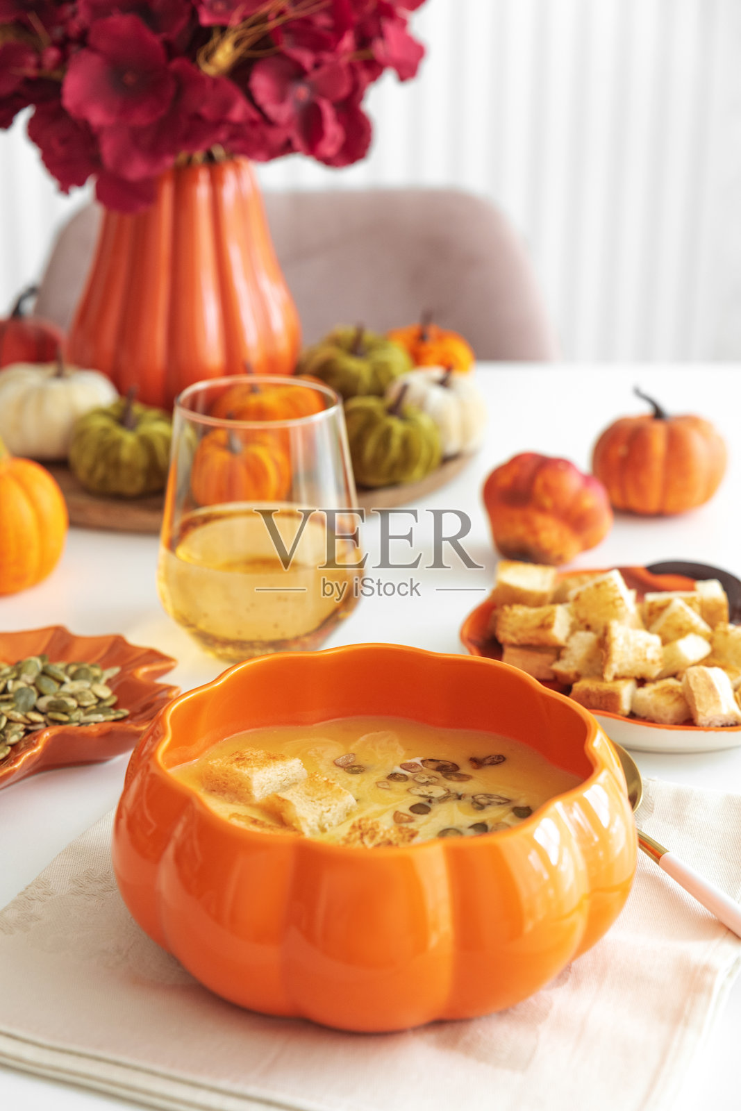 奶油南瓜汤配面包丁和南瓜籽,盛放在南瓜形状的碗里,放在白色的木桌上。照片摄影图片