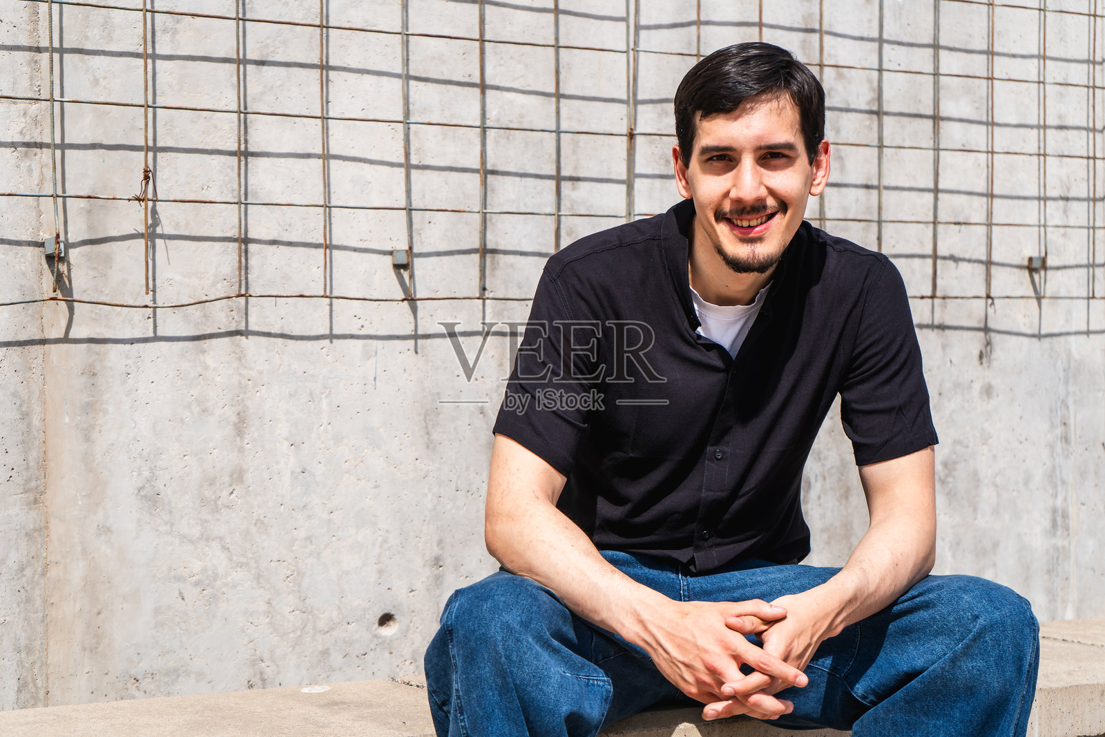 年轻男子面带微笑坐在城市环境中照片摄影图片