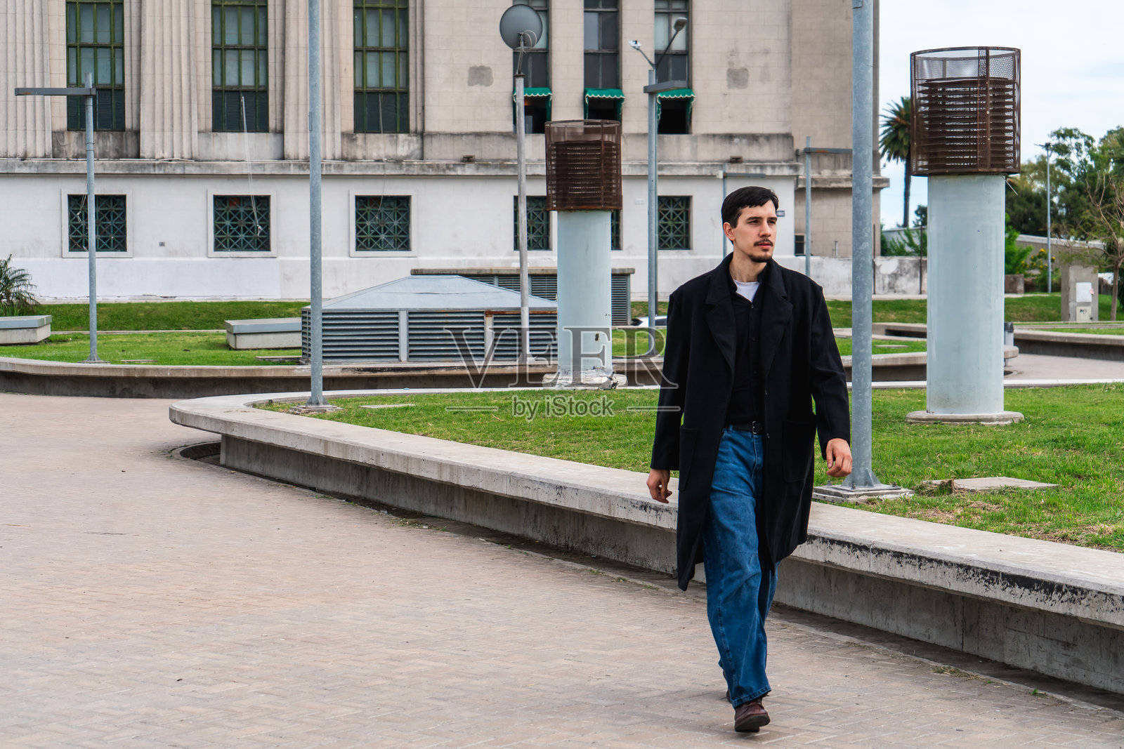 穿着大衣的年轻男子走过城市公园照片摄影图片