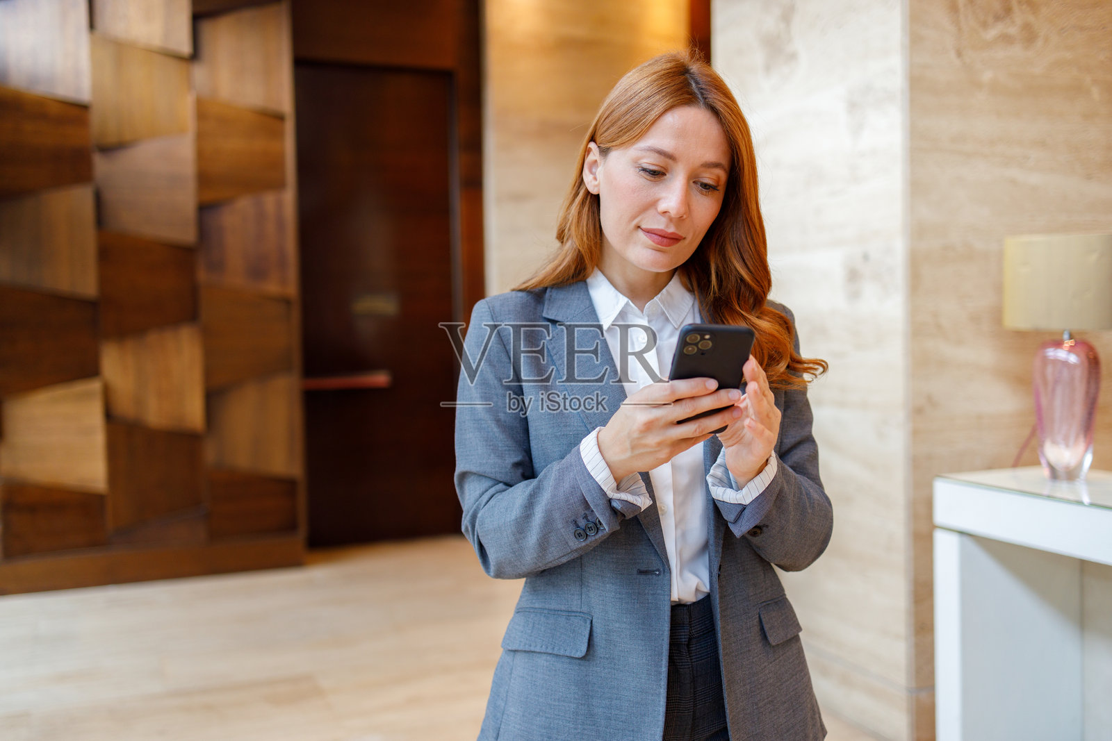 身着西装的专业女商人站在现代办公室大堂,使用手机进行沟通照片摄影图片