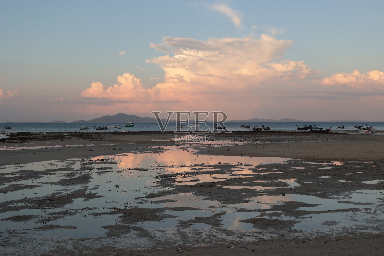 泰国日落时分,低潮后的空旷海滩,沙质海床和浅水区,映衬着戏剧性的橙粉色云彩照片摄影图片