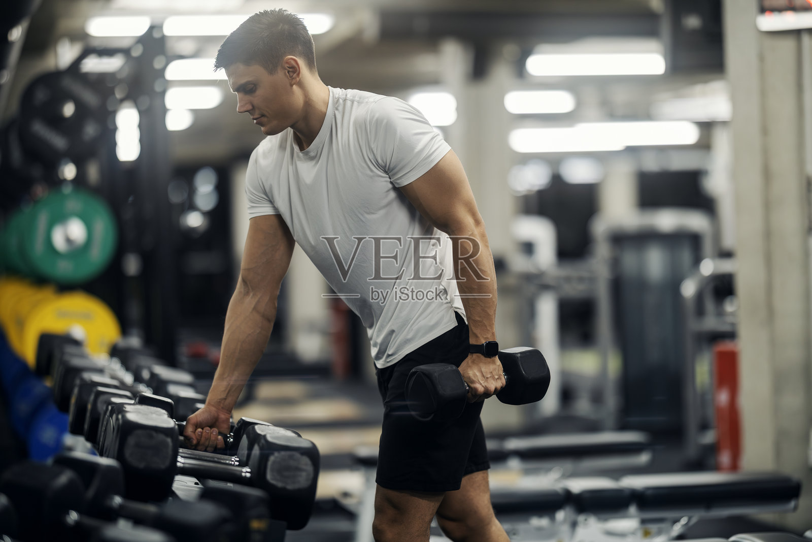 年轻男子在健身房准备进行哑铃锻炼照片摄影图片