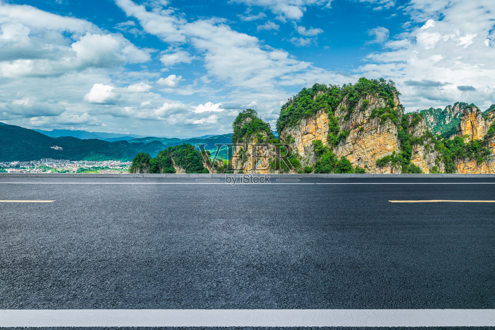 蓝天下,绿色的山峦构成了一幅风景画,一望无际的柏油路延伸向前。照片摄影图片