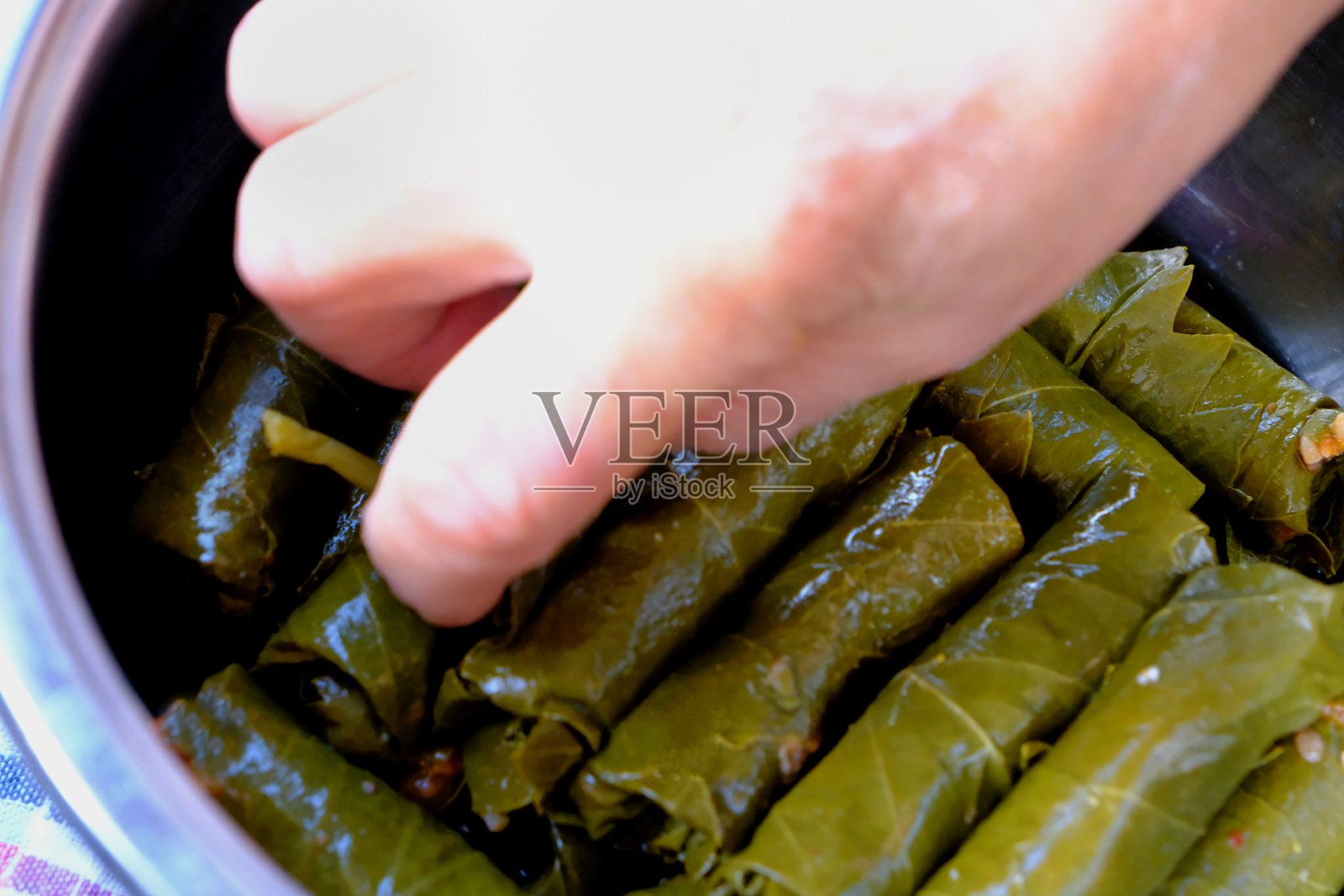 特写:女性双手正在锅中摆放自制的酿葡萄叶。照片摄影图片