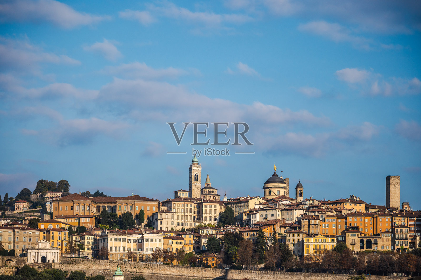 意大利贝加莫高地全景,展示了色彩缤纷的历史建筑、教堂塔楼和古老城墙,背景是明亮的蓝天照片摄影图片