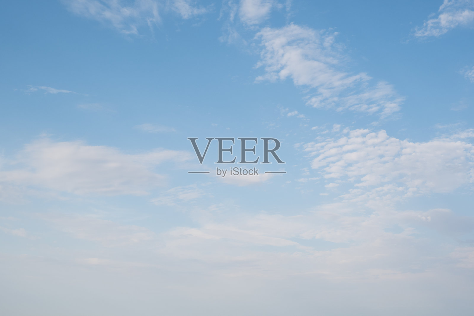 晴朗的天空点缀着几朵白云。云朵大小和形状各异,营造出宁静祥和的氛围。背景为浅蓝色。照片摄影图片