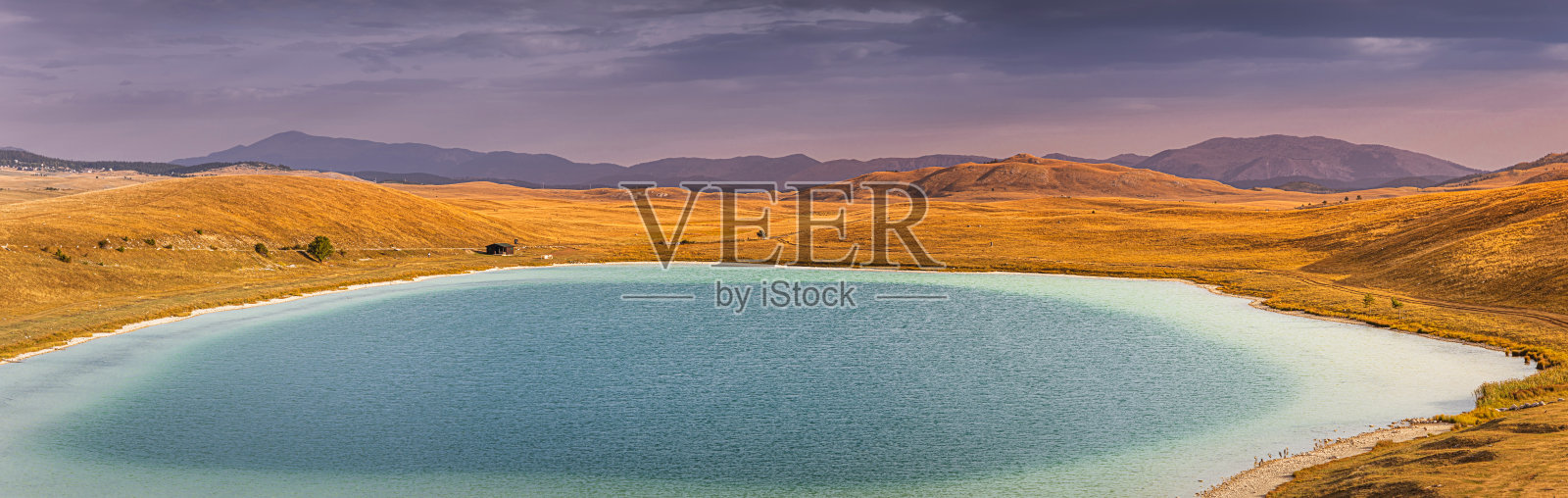 平静的绿松石湖泊,四周环绕着金色的山丘和远处的山脉,倒映着戏剧般的天空,营造出宁静祥和的景象照片摄影图片