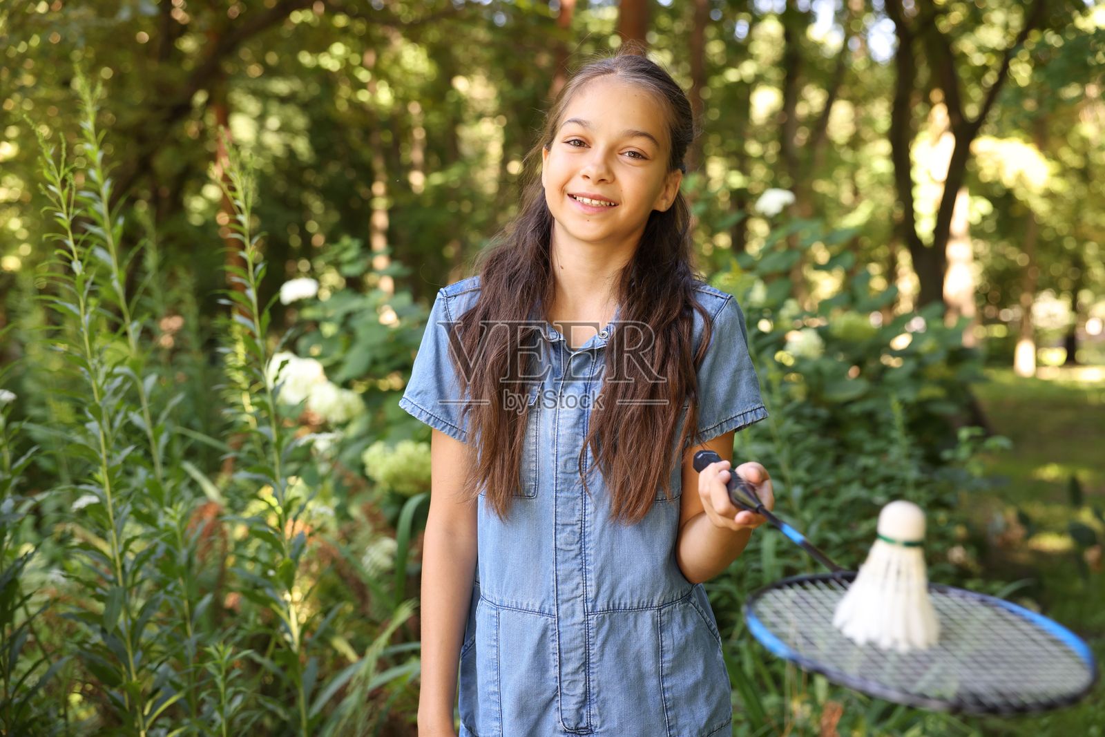 公园里,一位微笑着的小女孩拿着羽毛球拍和羽毛球的肖像照片摄影图片