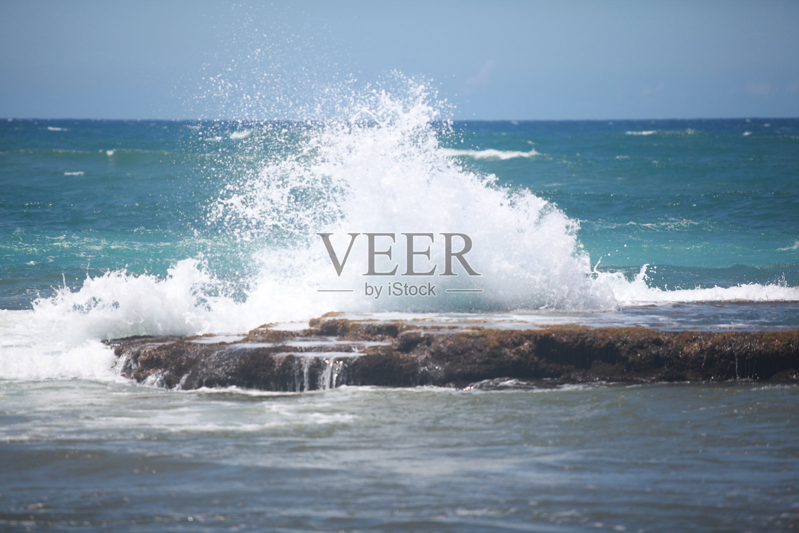 阳光明媚的日子里,海浪拍打着岩石海岸,溅起美丽的海沫。照片摄影图片