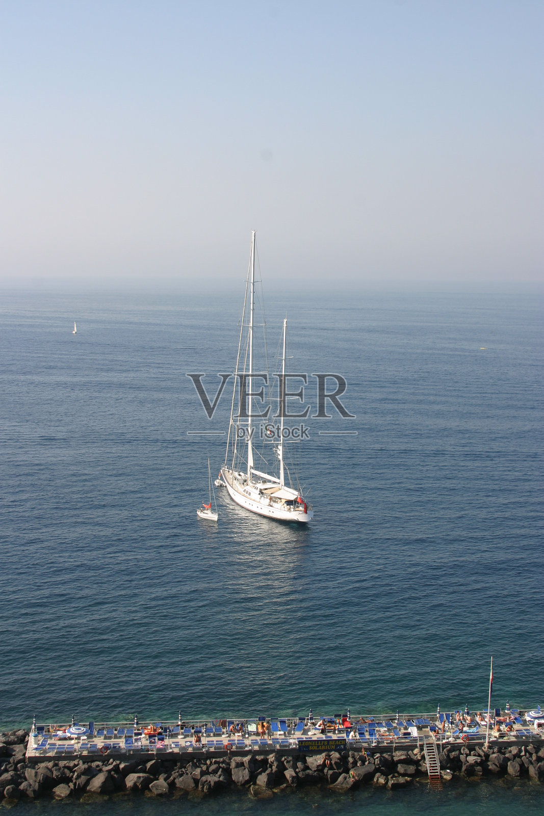 帆船在明媚的午后阳光下,于宁静水域上靠近海岸码头滑行照片摄影图片