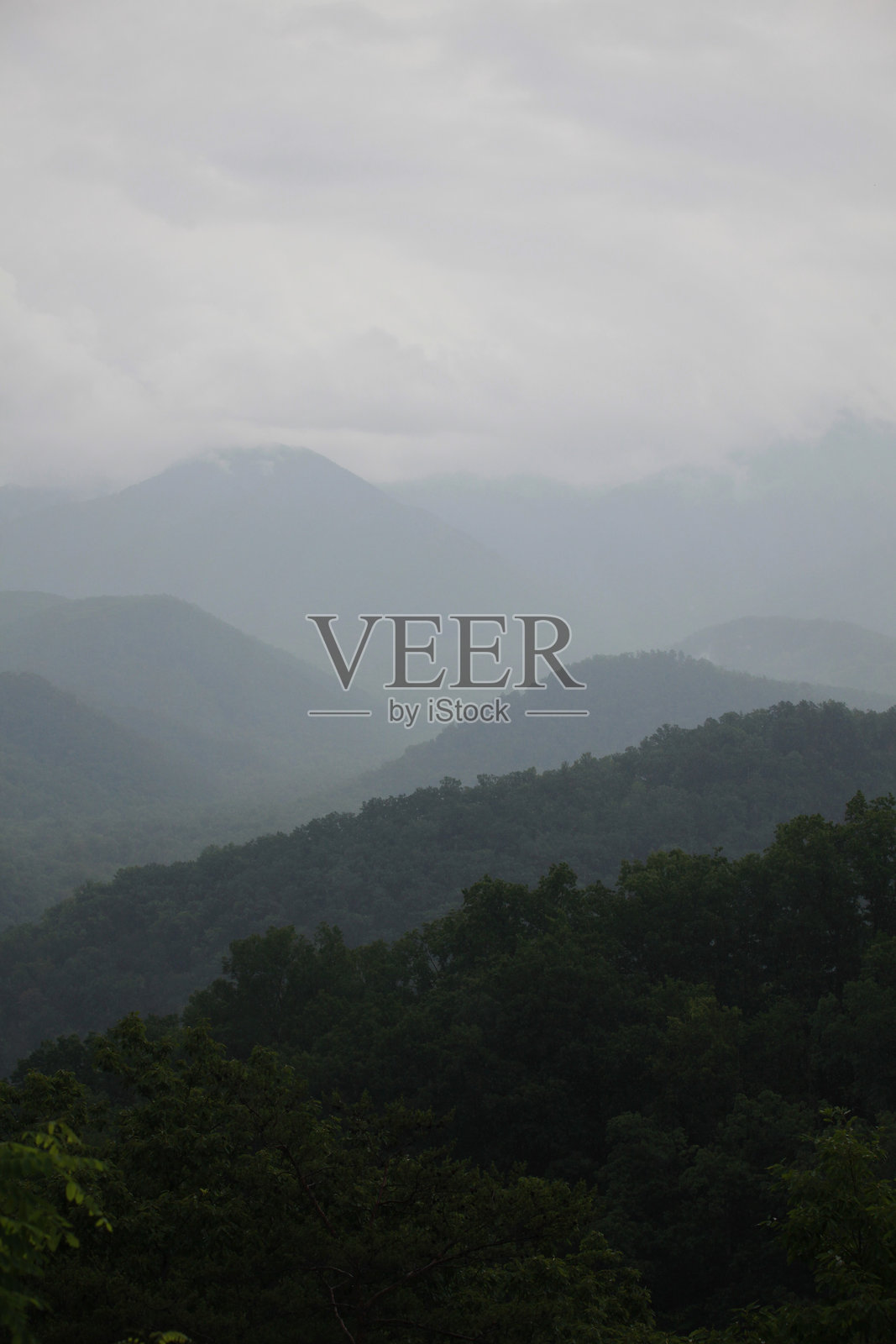 清晨时分,雾气缭绕的山峦层叠,天空布满阴云。照片摄影图片