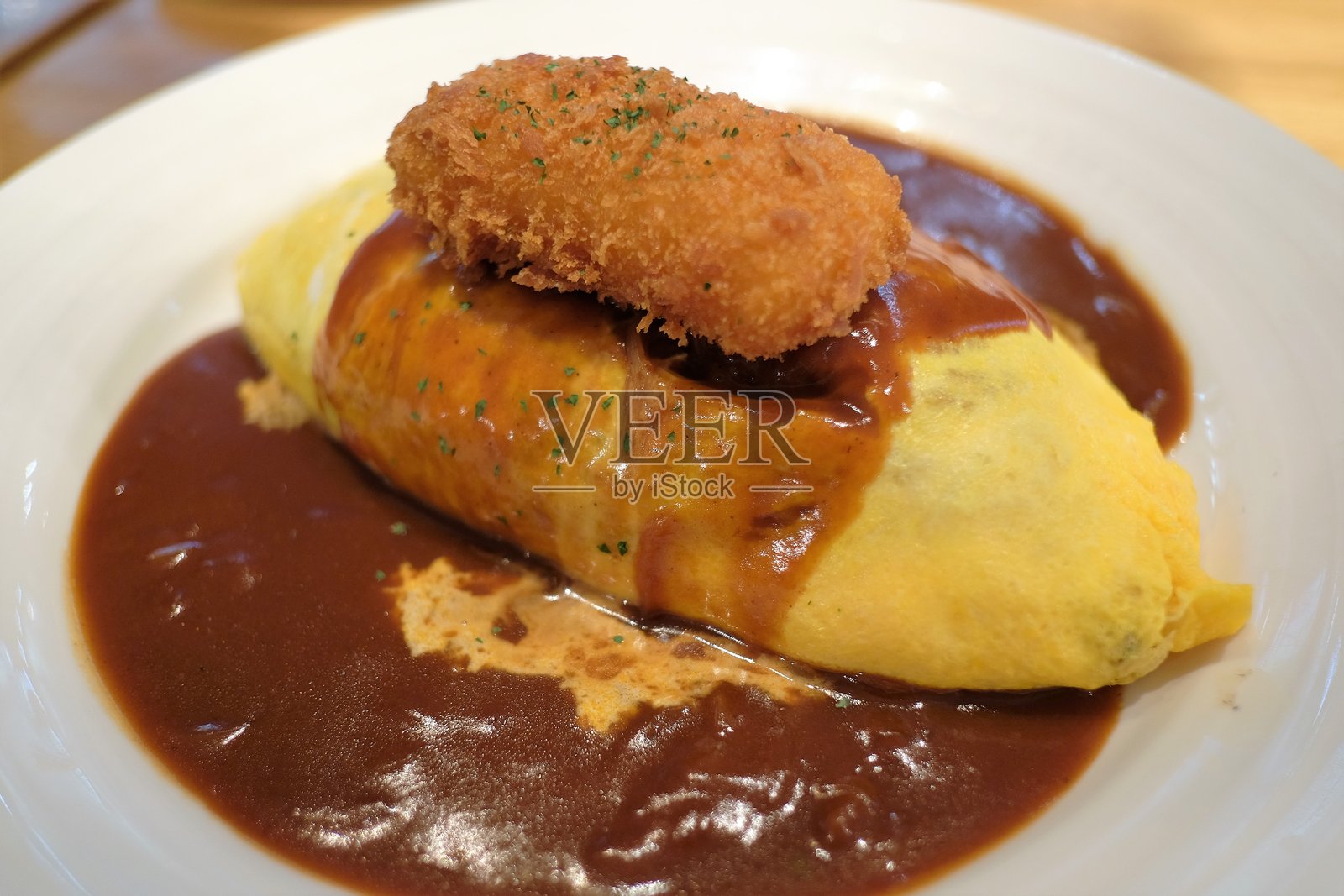 日式蛋包饭(米饭填充或包裹的日式煎蛋卷),配以辛辣、软糯、浓郁的咖喱酱,上面铺有炸三文鱼。照片摄影图片