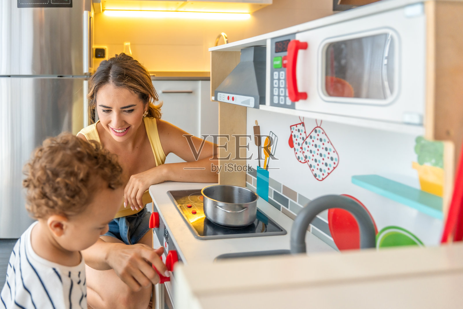 在现代公寓里,一位母亲和她的儿子在玩玩具厨房照片摄影图片