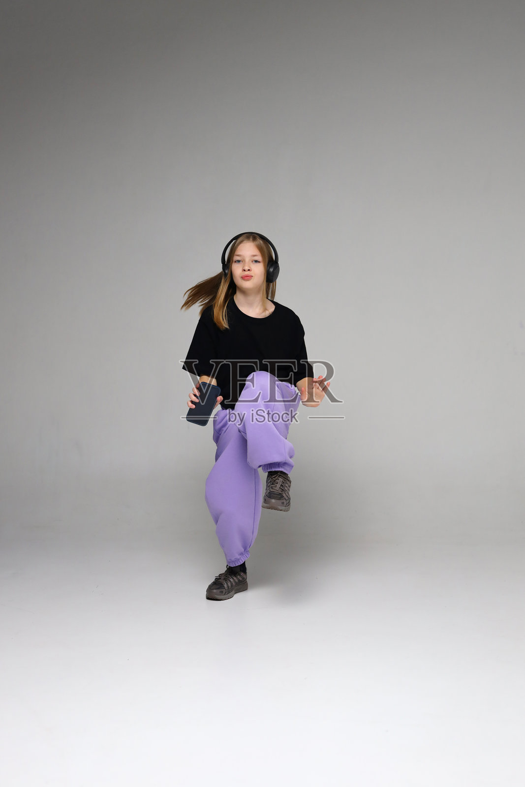年轻的白种人青少年女性戴着耳机、穿着紫色裤子在工作室里跳舞照片摄影图片