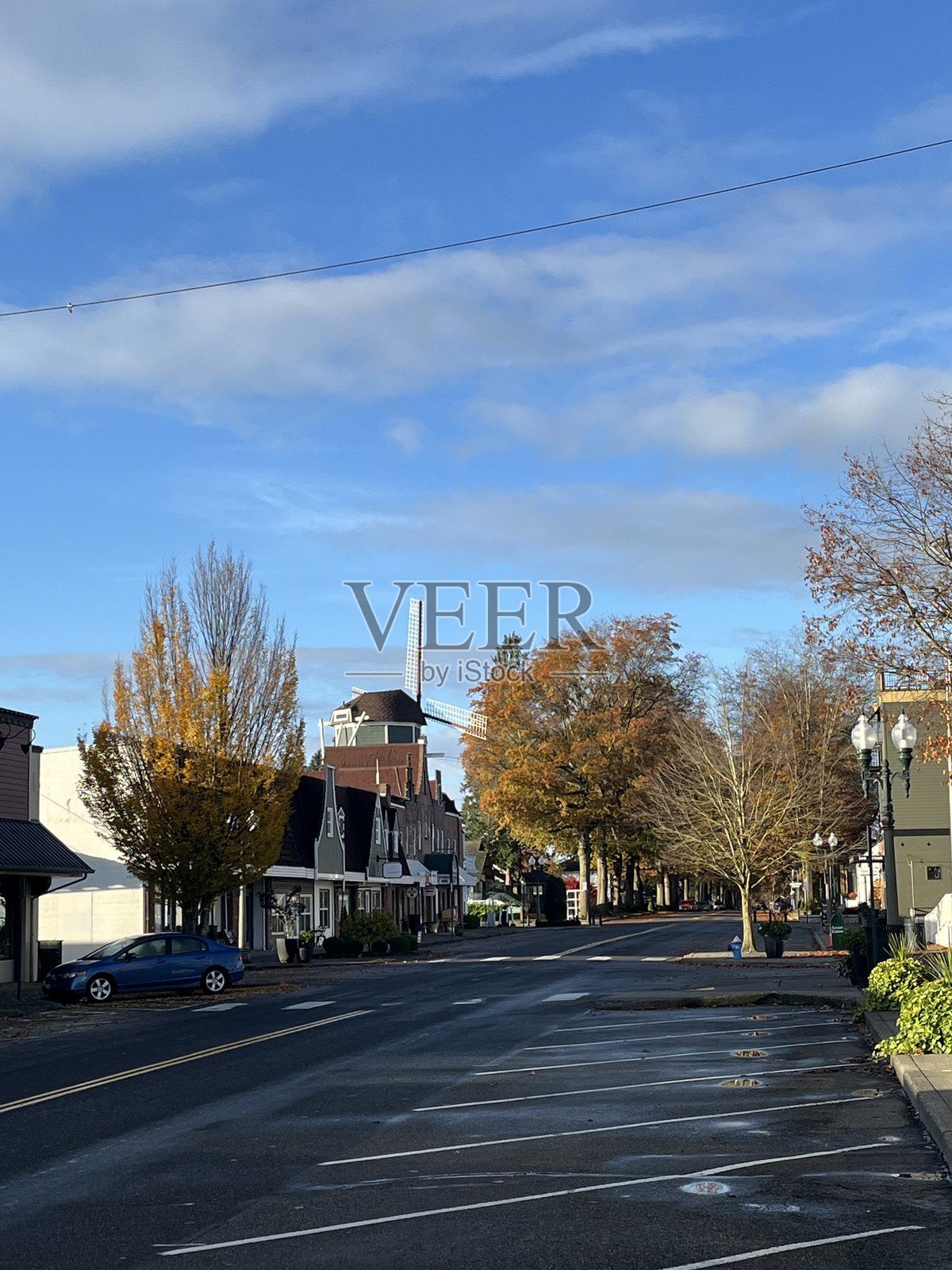 宁静的小镇街道,天空湛蓝,白云朵朵。路边是色彩斑斓的秋季树木,几栋建筑为街景增添了特色。照片摄影图片