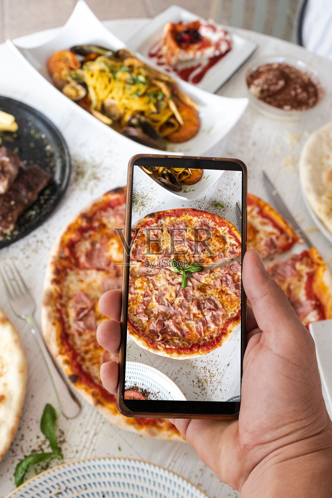 手持智能手机拍摄餐厅餐桌上的披萨照片摄影图片