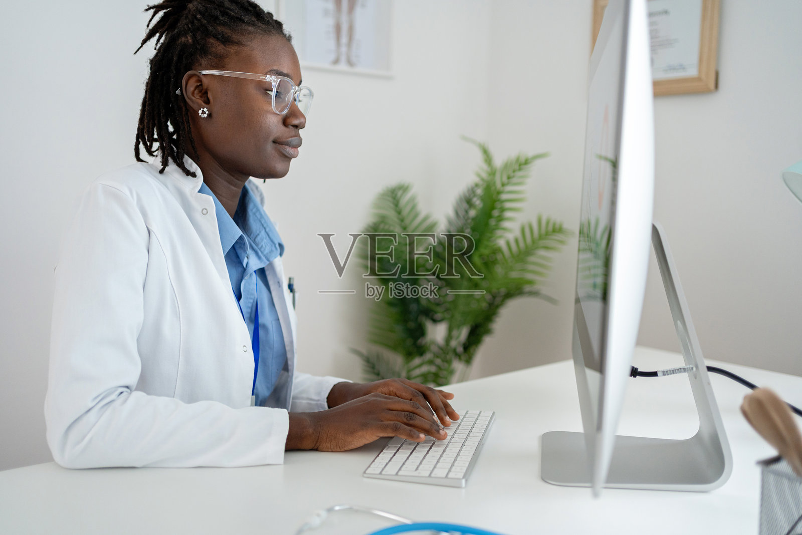 身穿白大褂、专注的年轻黑人女医生正在办公桌前打字照片摄影图片