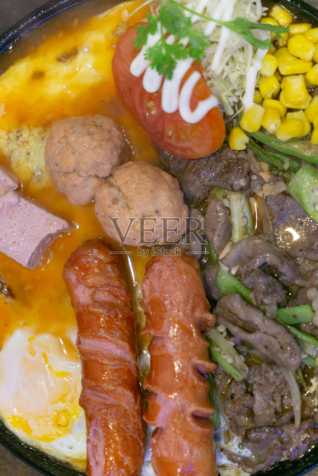 色彩鲜艳的什锦菜特写,包含香肠、肉丸、牛肉片、煎蛋、玉米、番茄配蛋黄酱,并用蔬菜点缀。照片摄影图片