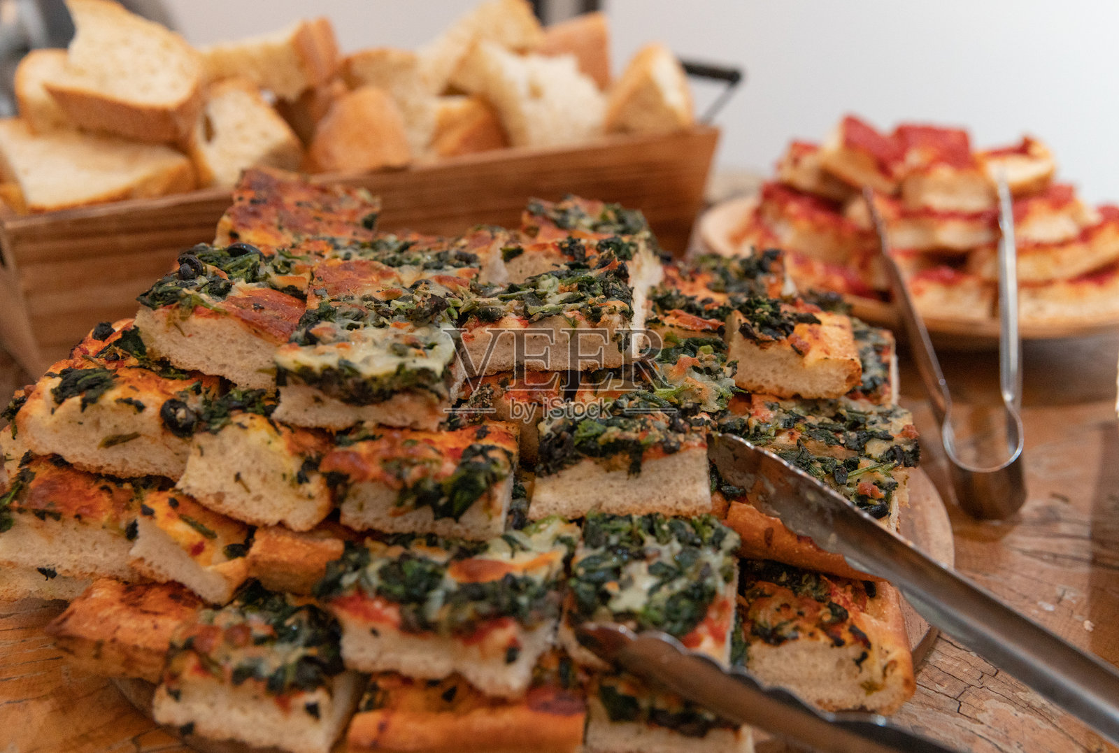 木板上堆叠着香草菠菜佛卡夏方块,旁边还有面包和开胃菜照片摄影图片