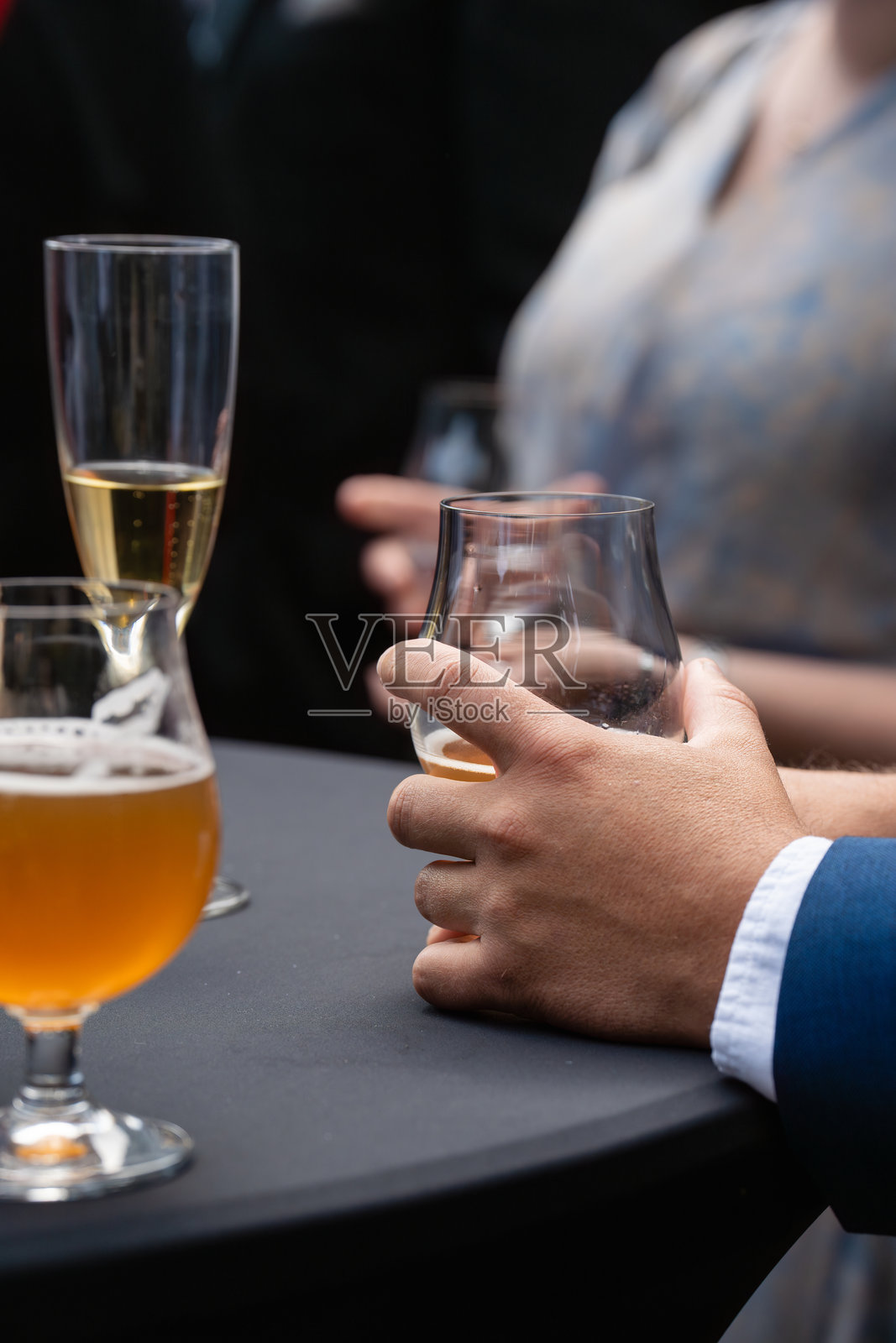 在精致的社交聚会或活动中,一只男人的手优雅地举着一杯琥珀色的精酿啤酒,特写镜头。照片摄影图片